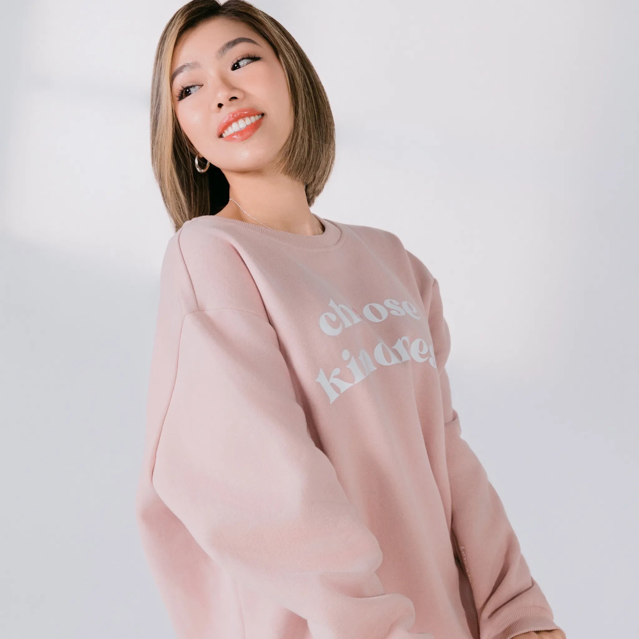 Woman wearing a pink sweatshirt with text on a plain background