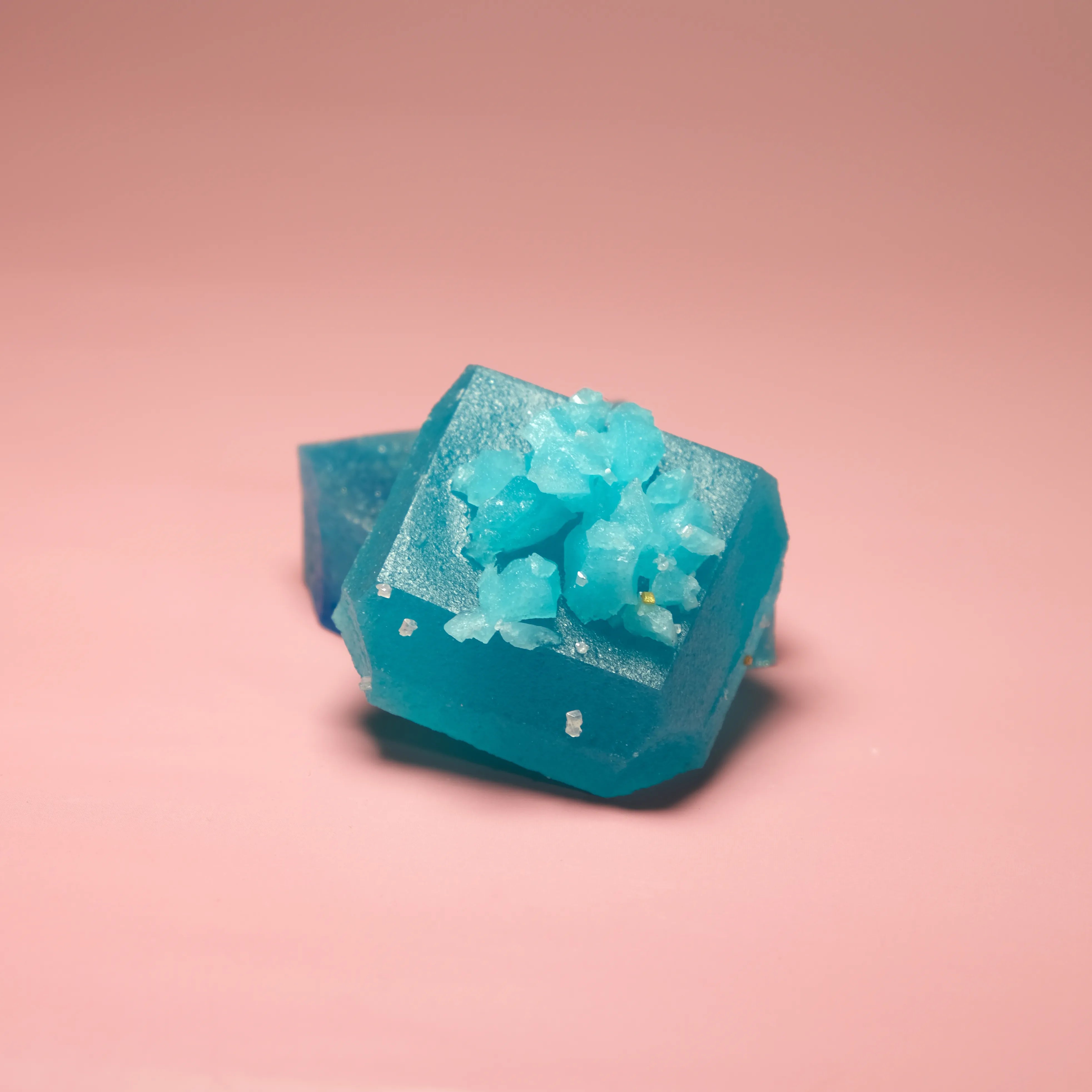 Blue raspberry flavored Silky Gem crystal candy with a translucent blue body and crystallized sugar topping on a pink background.