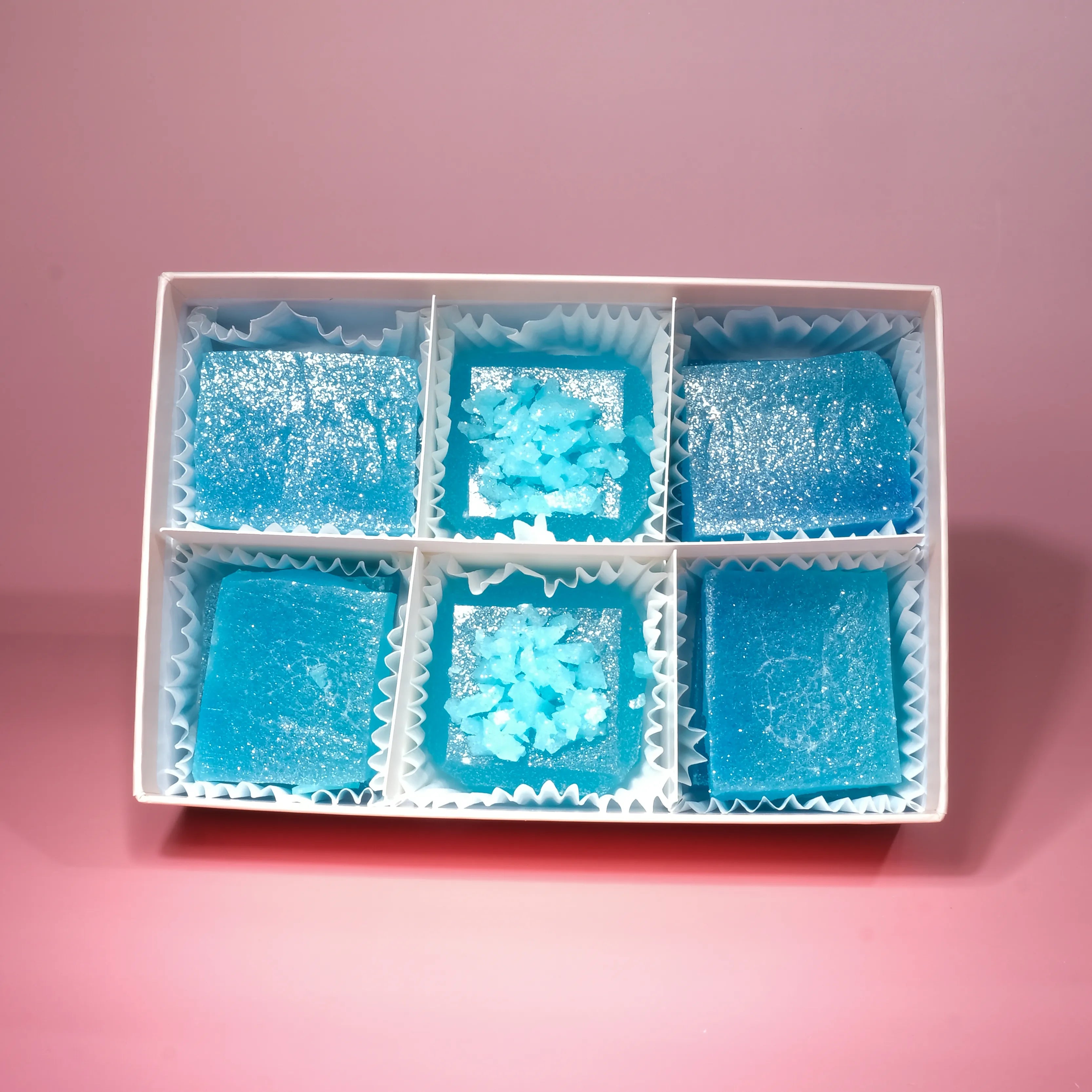 Box of six Blue Raspberry Lapis Silky Gem crystal candies arranged in paper liners, featuring glittering sugar tops and vibrant blue crystal textures.