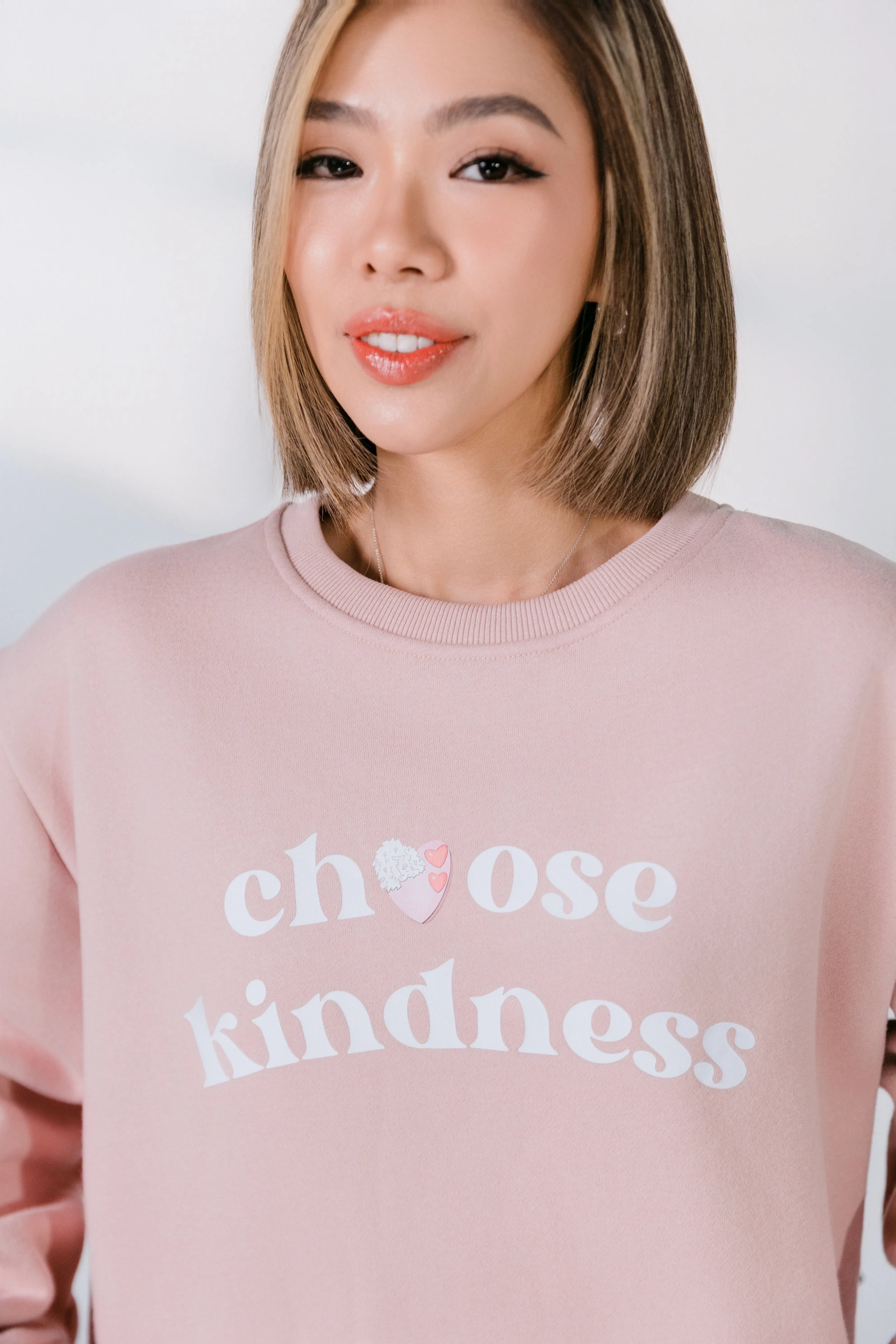Person wearing a pink sweatshirt with 'choose kindness' text