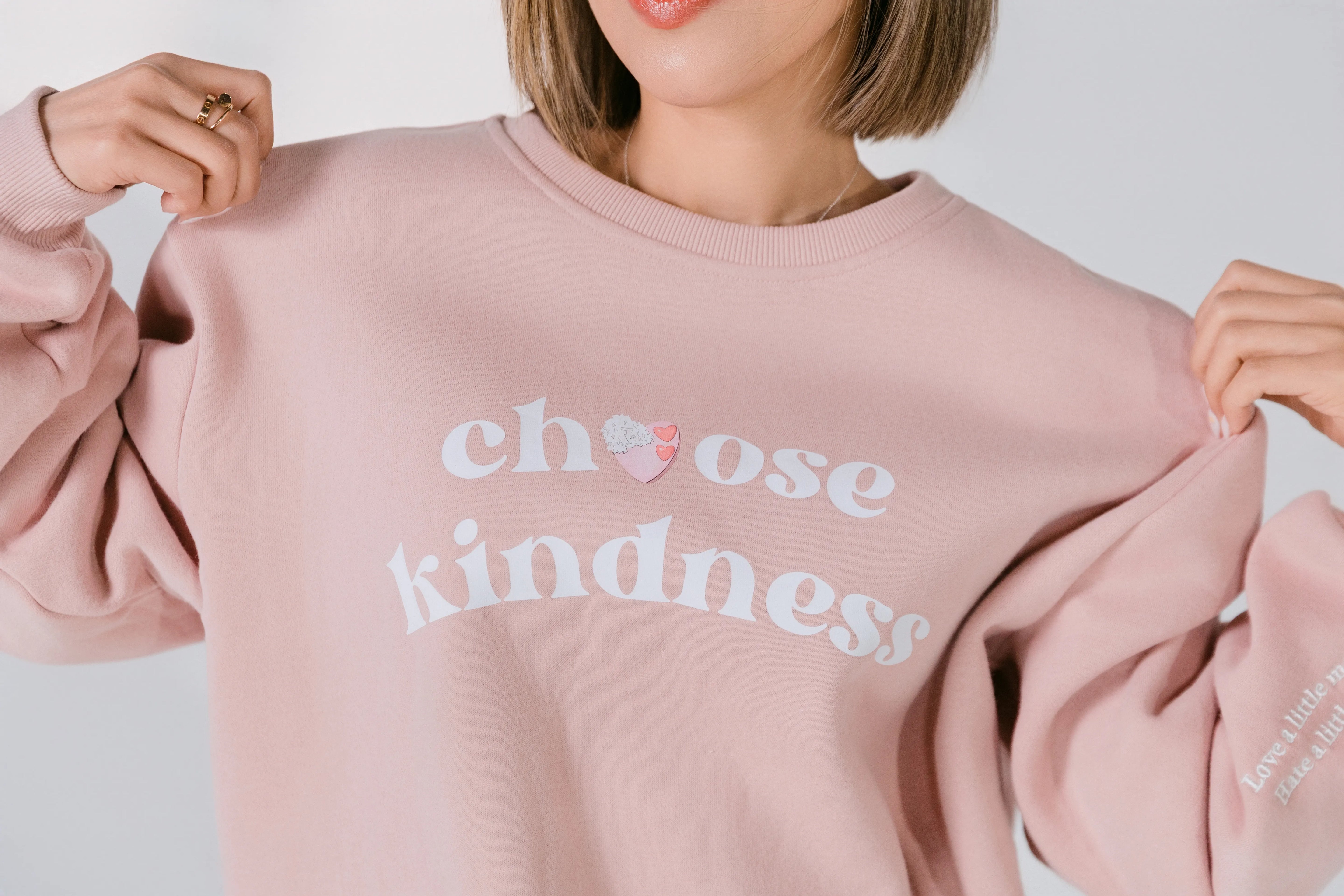 Close-up of white “Choose Kindness” graphic with heart detail on blush pink fabric.