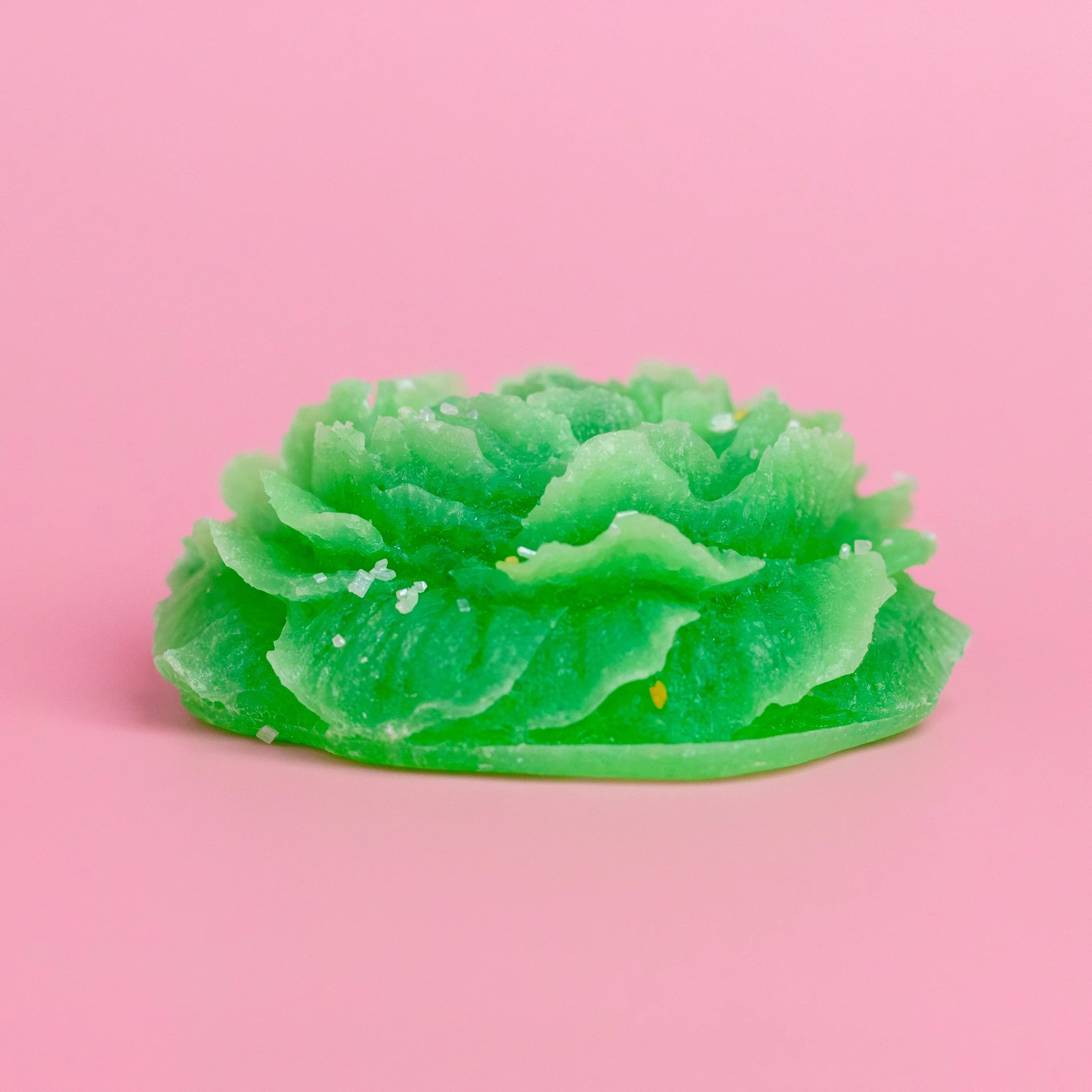 Green floral-shaped wax melt on a pink background