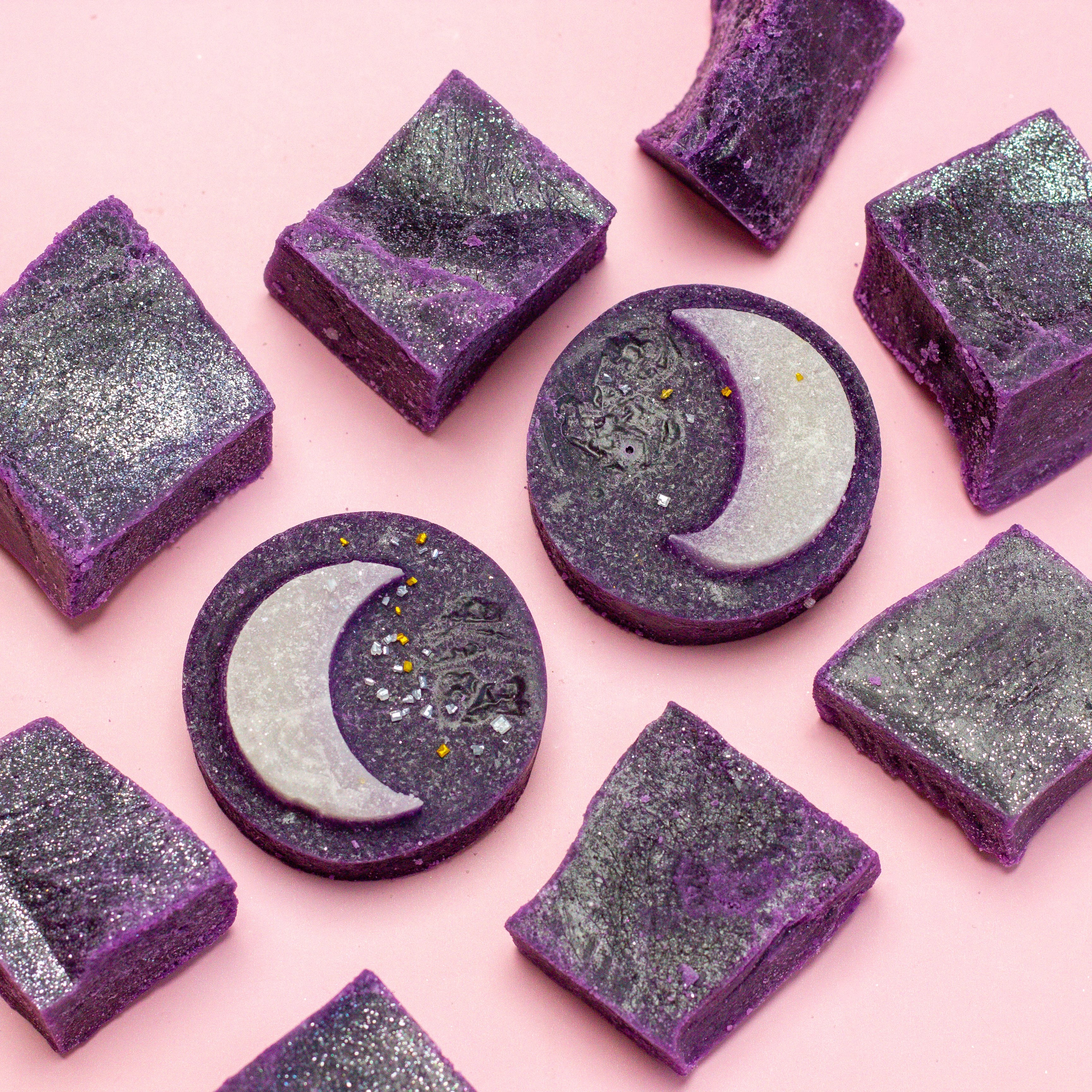 Purple and gray soap bars with moon designs on a pink background