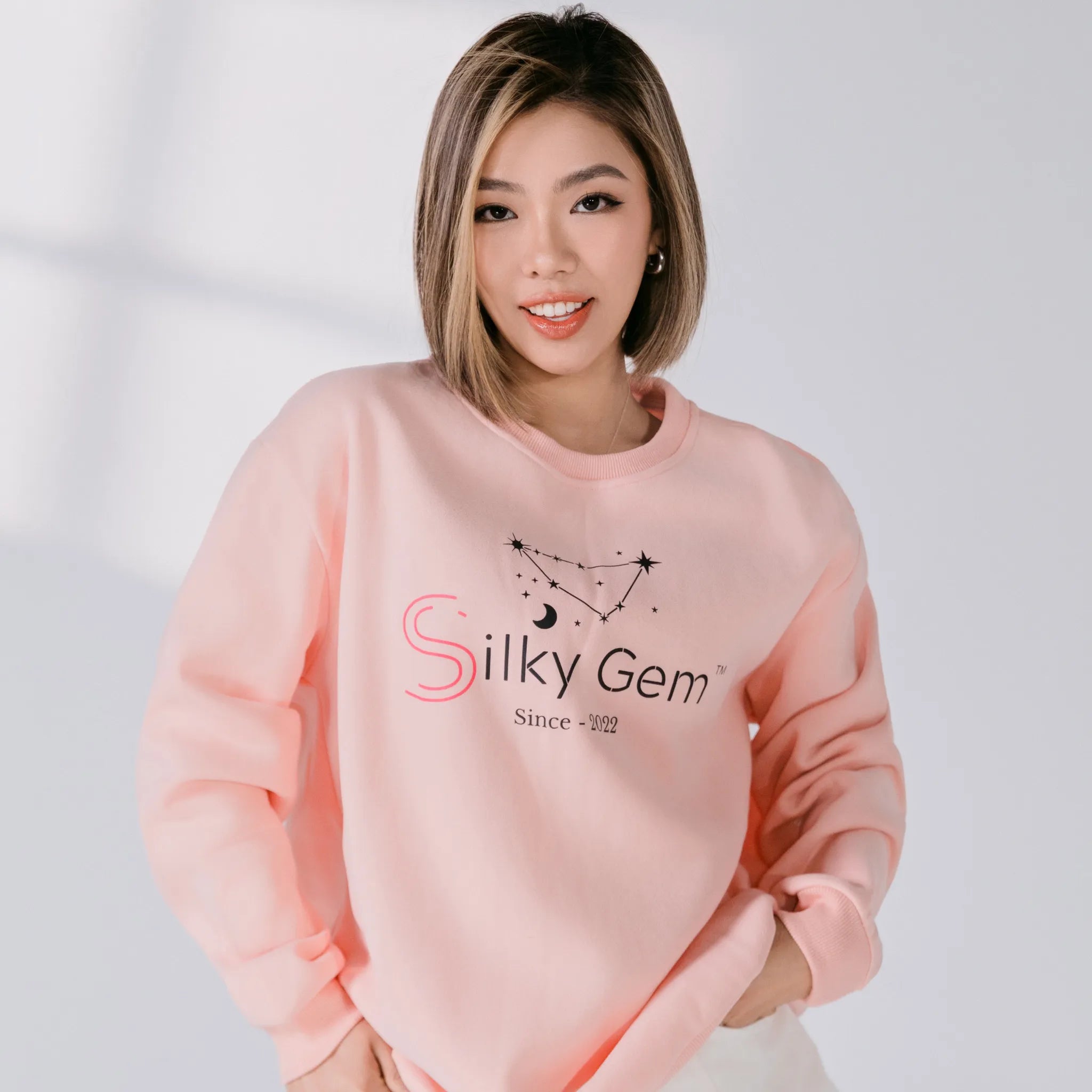 Person wearing a pink sweatshirt with 'Silky Gem' logo on a white background