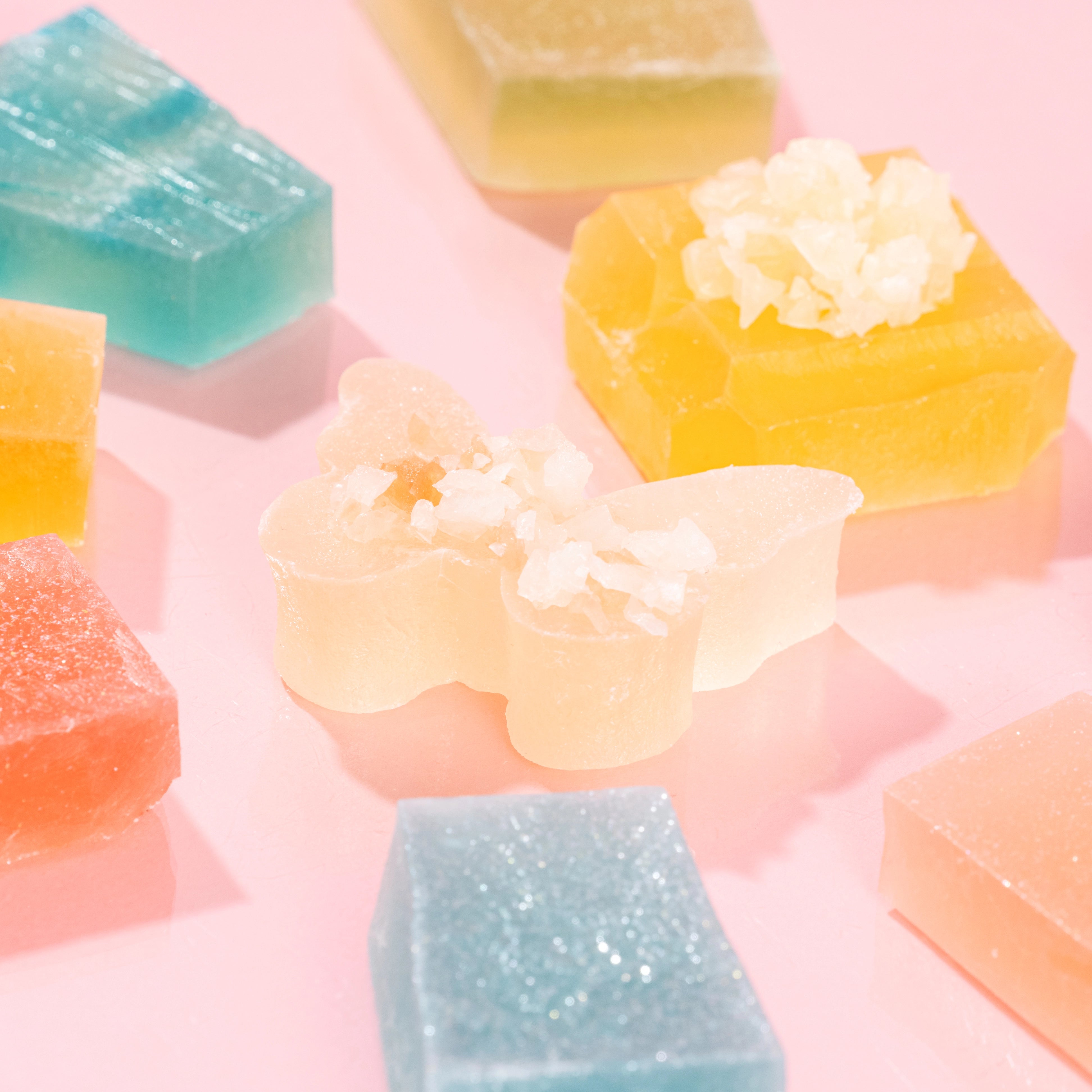 Close-up of assorted butterfly and gem-shaped Silky Gem crystal candies from The Gemmies Collection, displayed on a pink background.