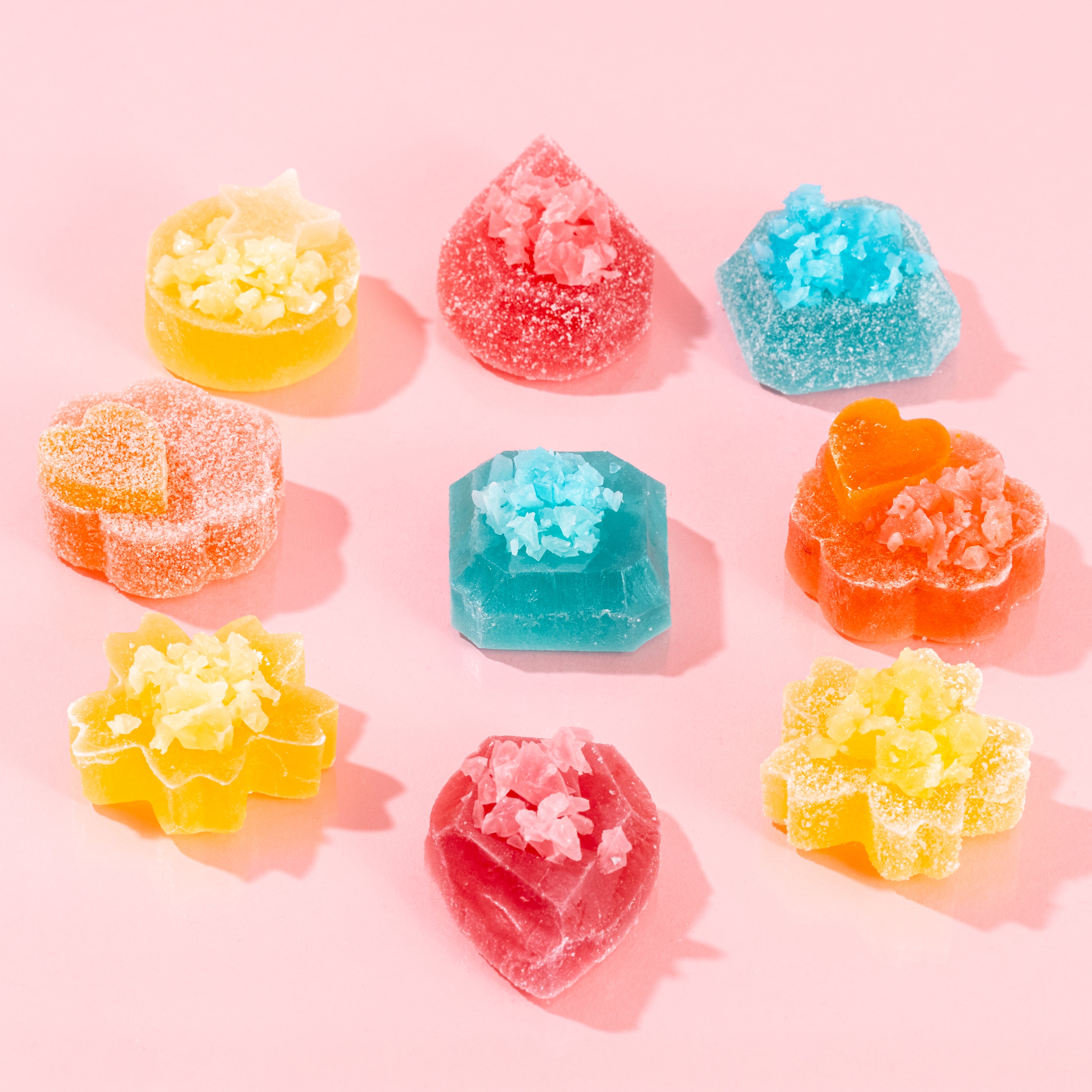 Close-up of vibrant Silky Gem crystal candy pieces from The Golden Lava collection, featuring assorted shapes on a pink background.