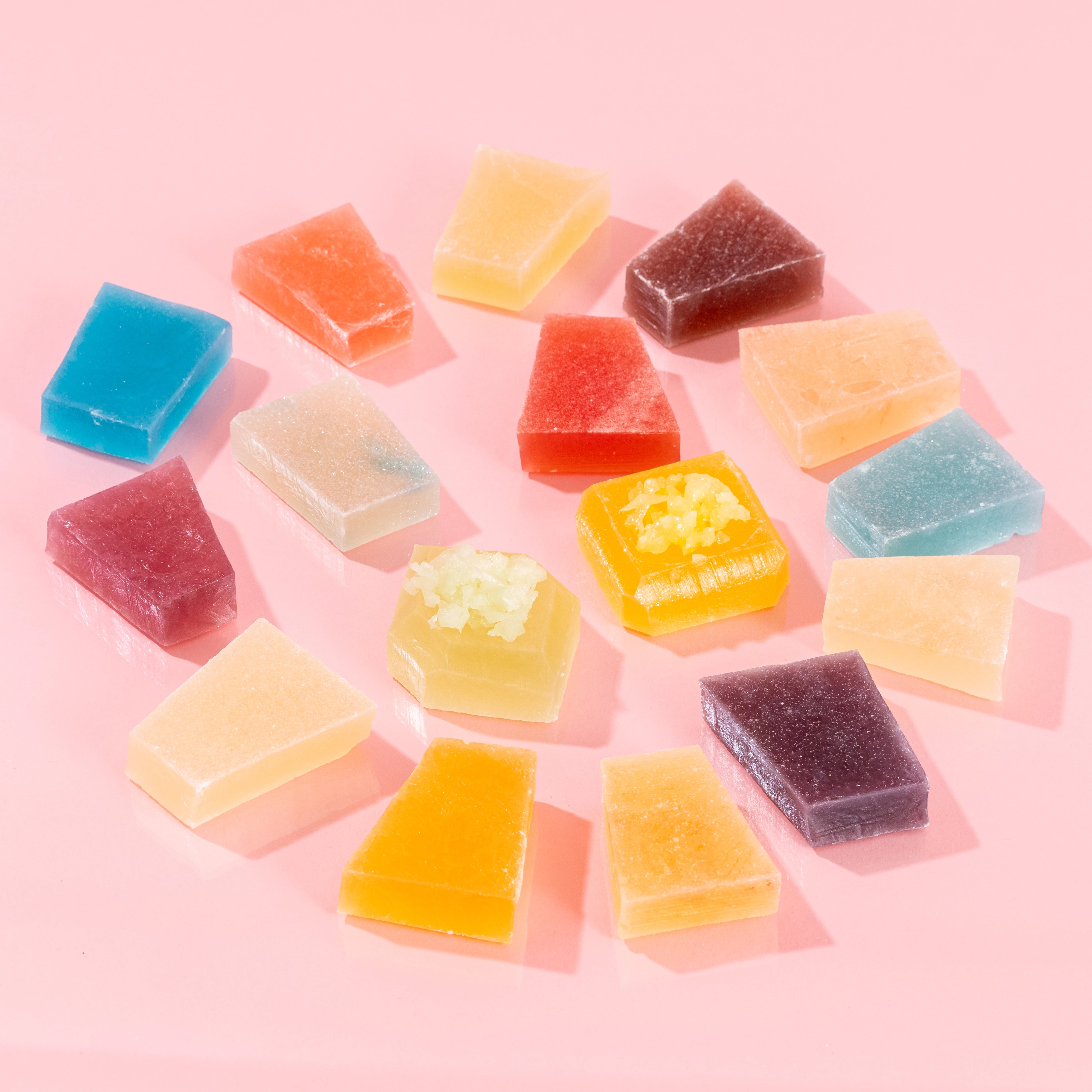 Close-up of vibrant, crystal-cut candy pieces from the Treasure Box collection, with some pieces cut in half to reveal the signature firm, jelly-like center, displayed on a pink background.
