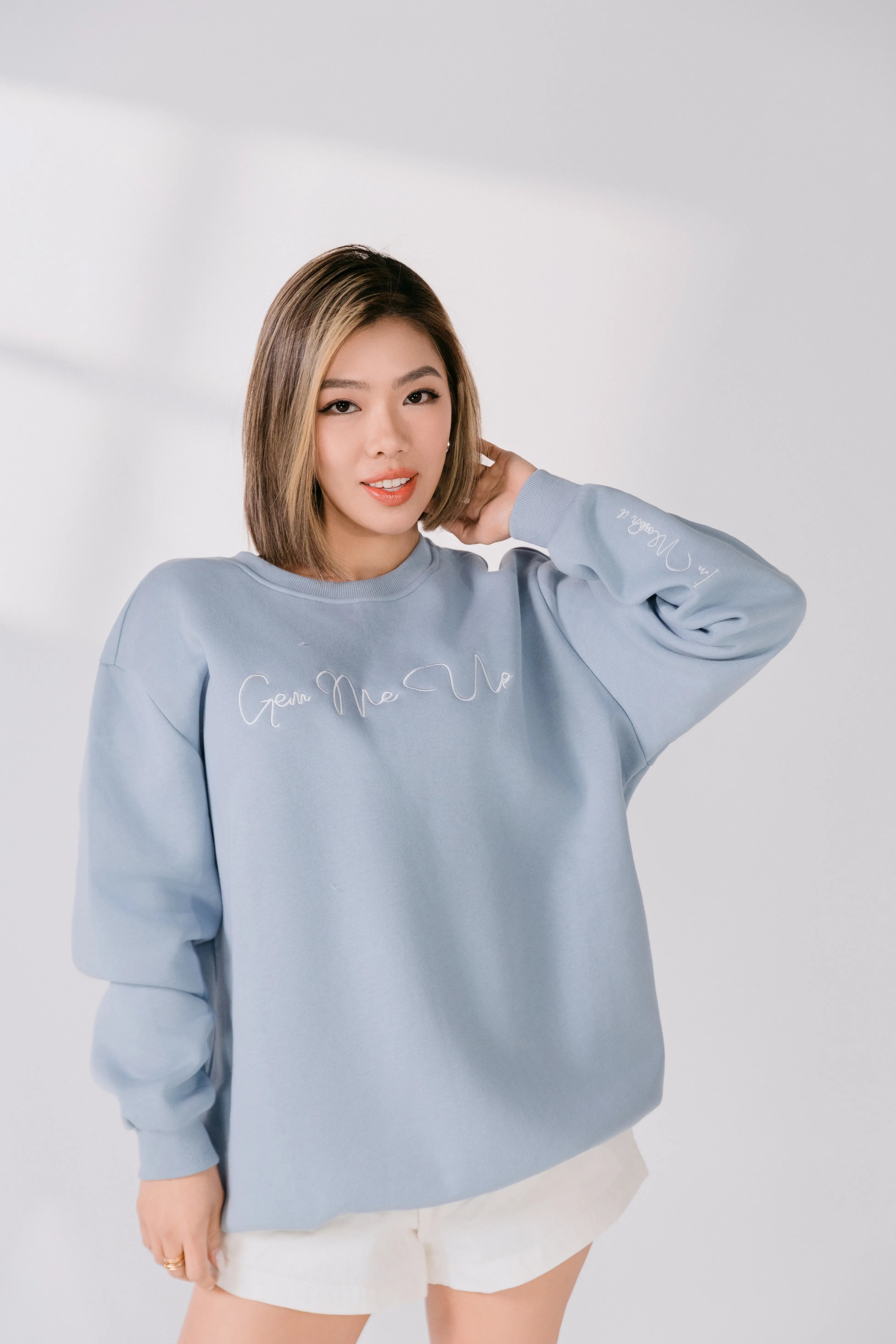 Lifestyle image of model smiling in powder blue Gem Me Up sweatshirt.