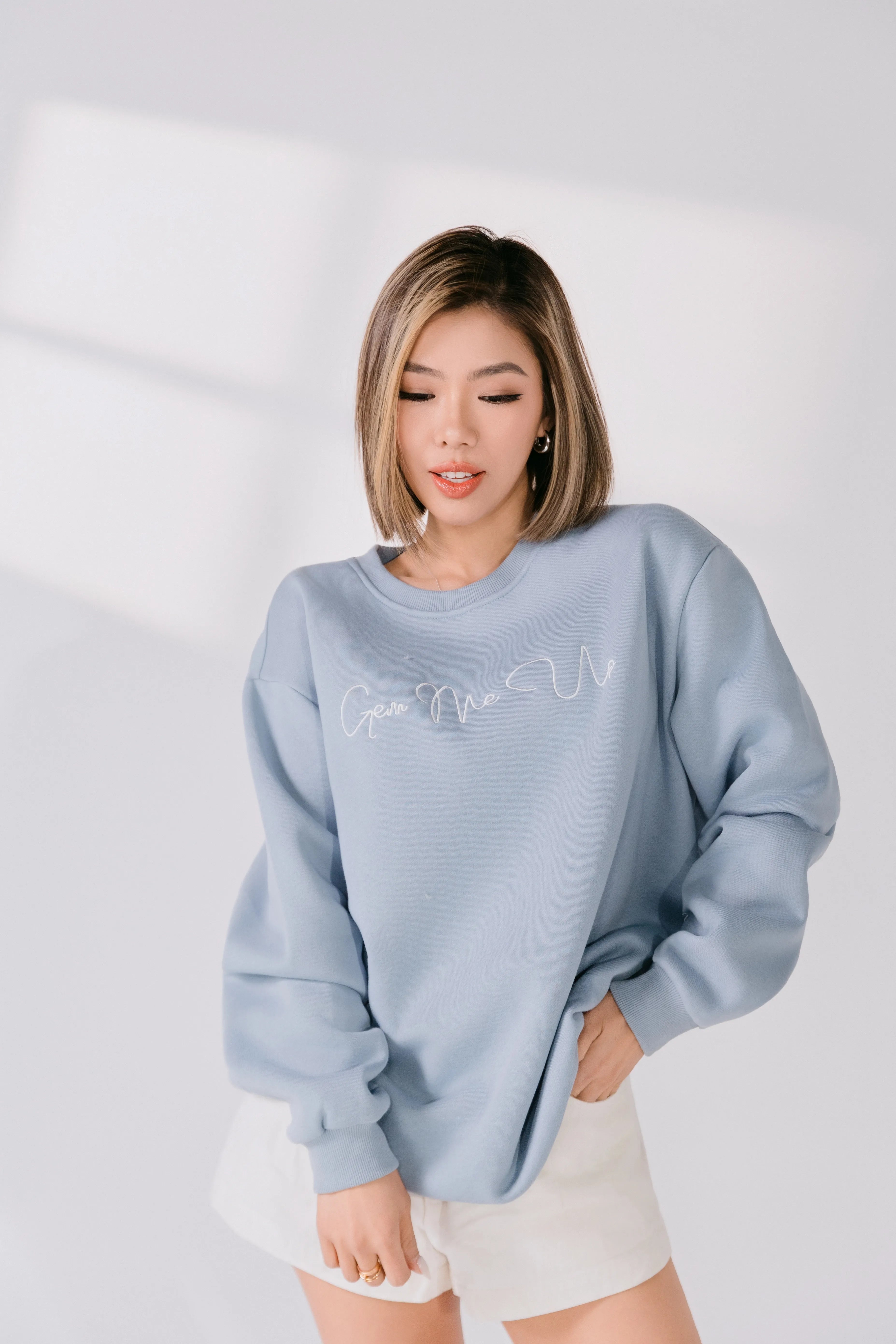 Close-up of white embroidered “Gem Me Up” script on powder blue fabric.