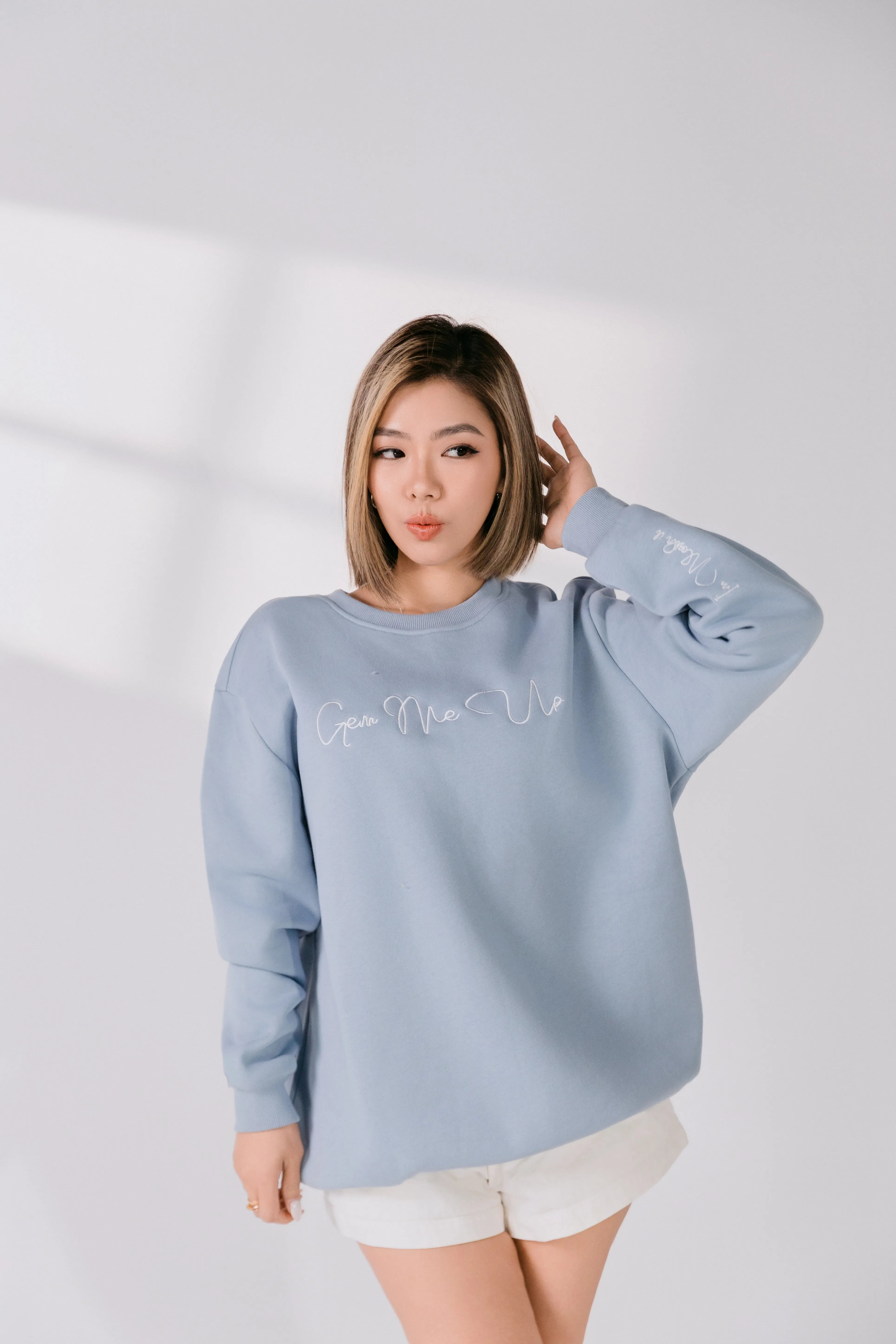 Model adjusting hair while wearing powder blue Gem Me Up sweatshirt.