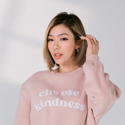 Woman wearing a pink sweatshirt with 'choose kindness' text on a white background