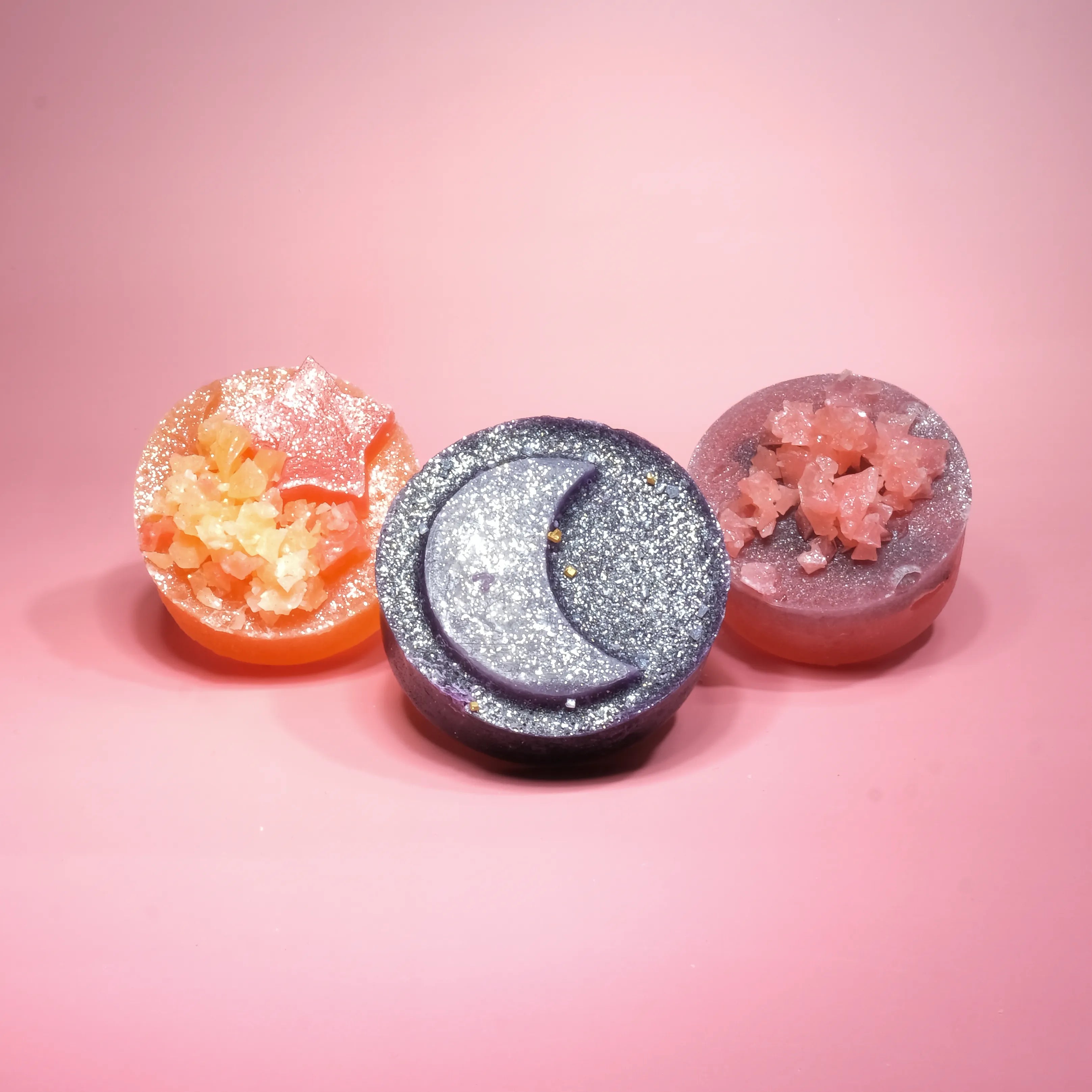 Three crystal candies on a pink background featuring a green teardrop candy, a yellow star-shaped candy, and a pink gemstone-shaped candy, each topped with shimmering sugar crystals.