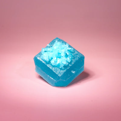 Single Blue Raspberry Lapis Silky Gem crystal candy with a faceted blue jelly exterior and icy sugar crystal center on a pink backdrop.