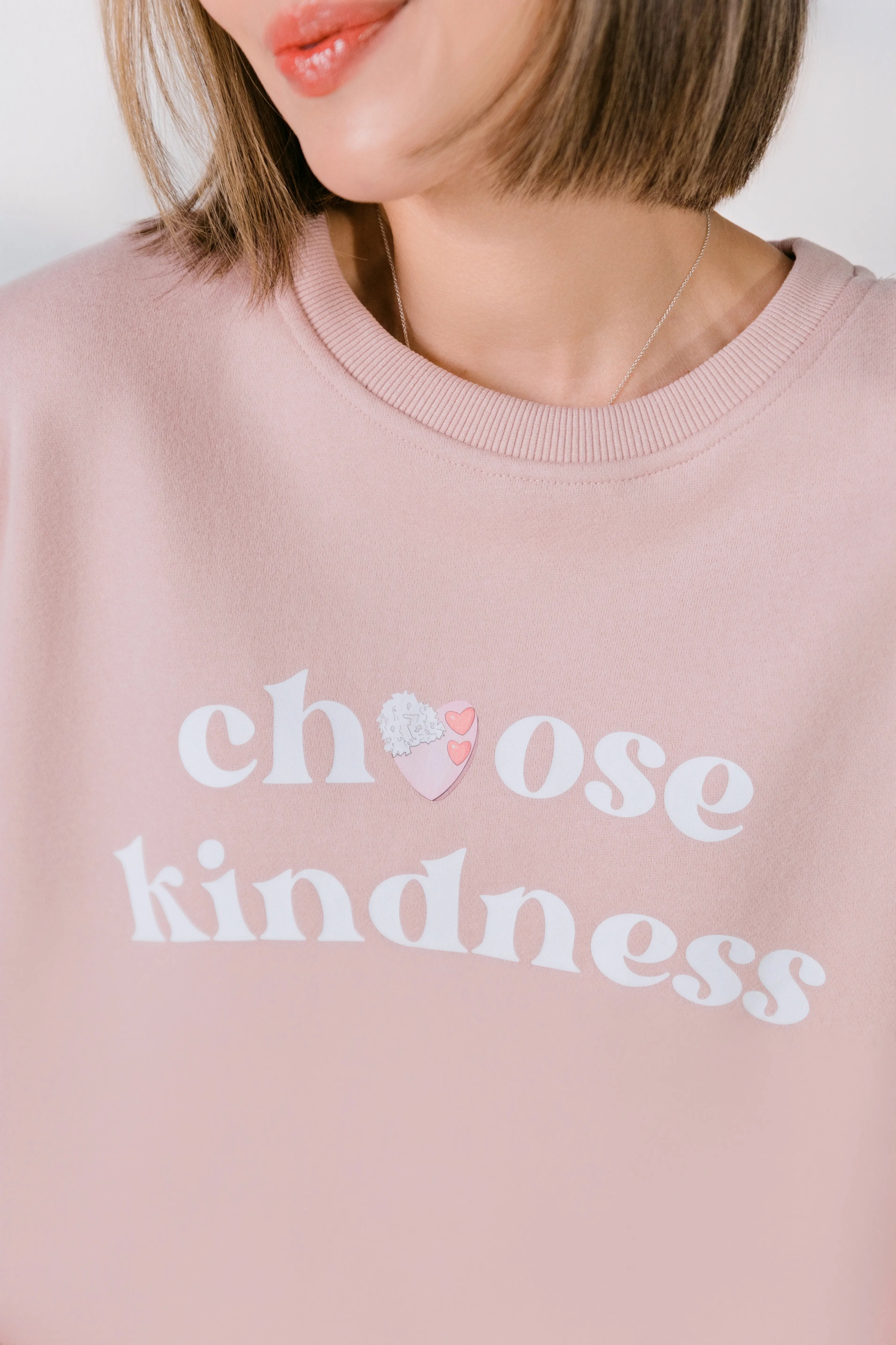 Detail of ribbed neckline and front graphic on blush pink sweatshirt.