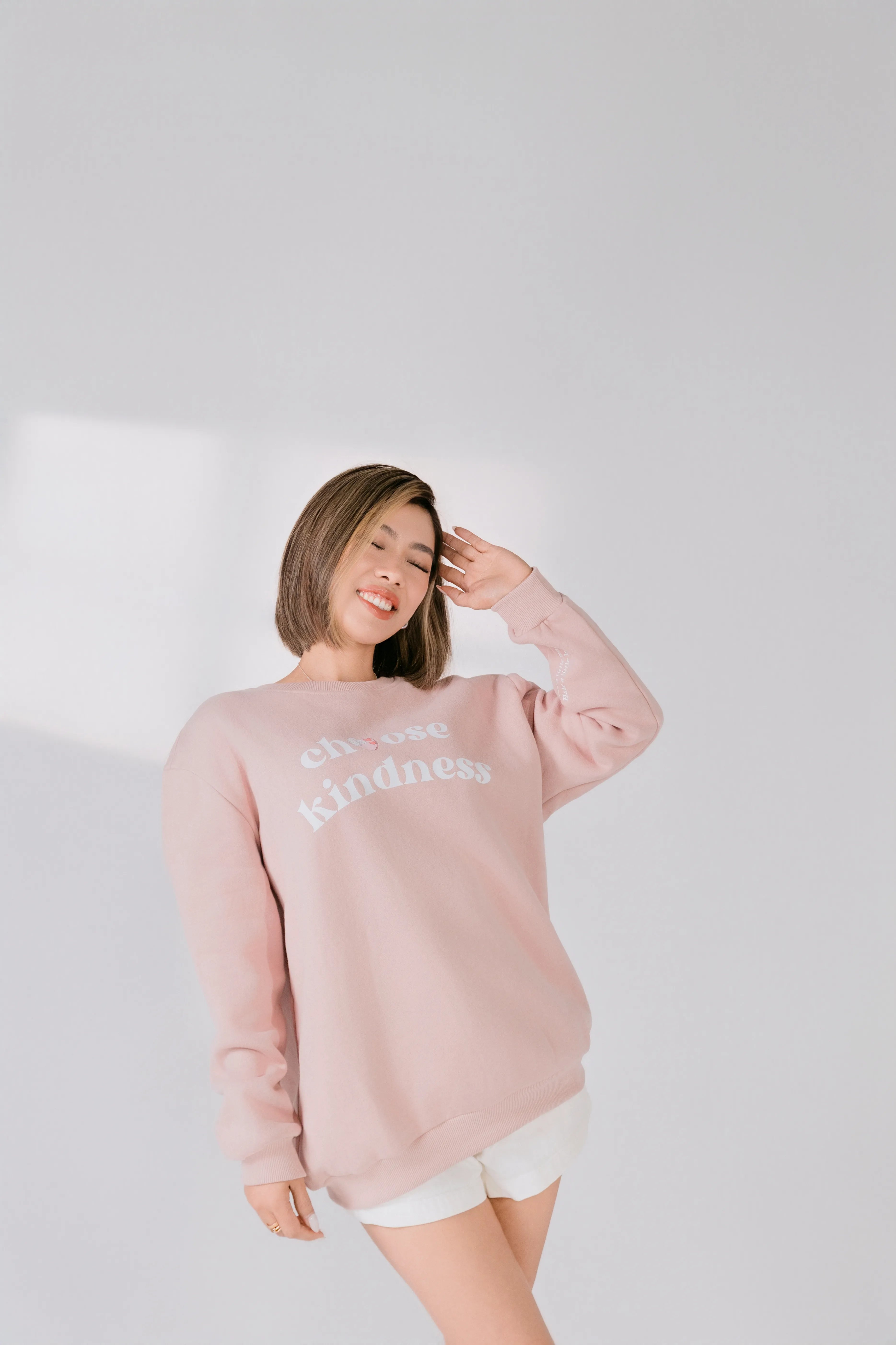Lifestyle image of model smiling while wearing blush pink graphic sweatshirt.