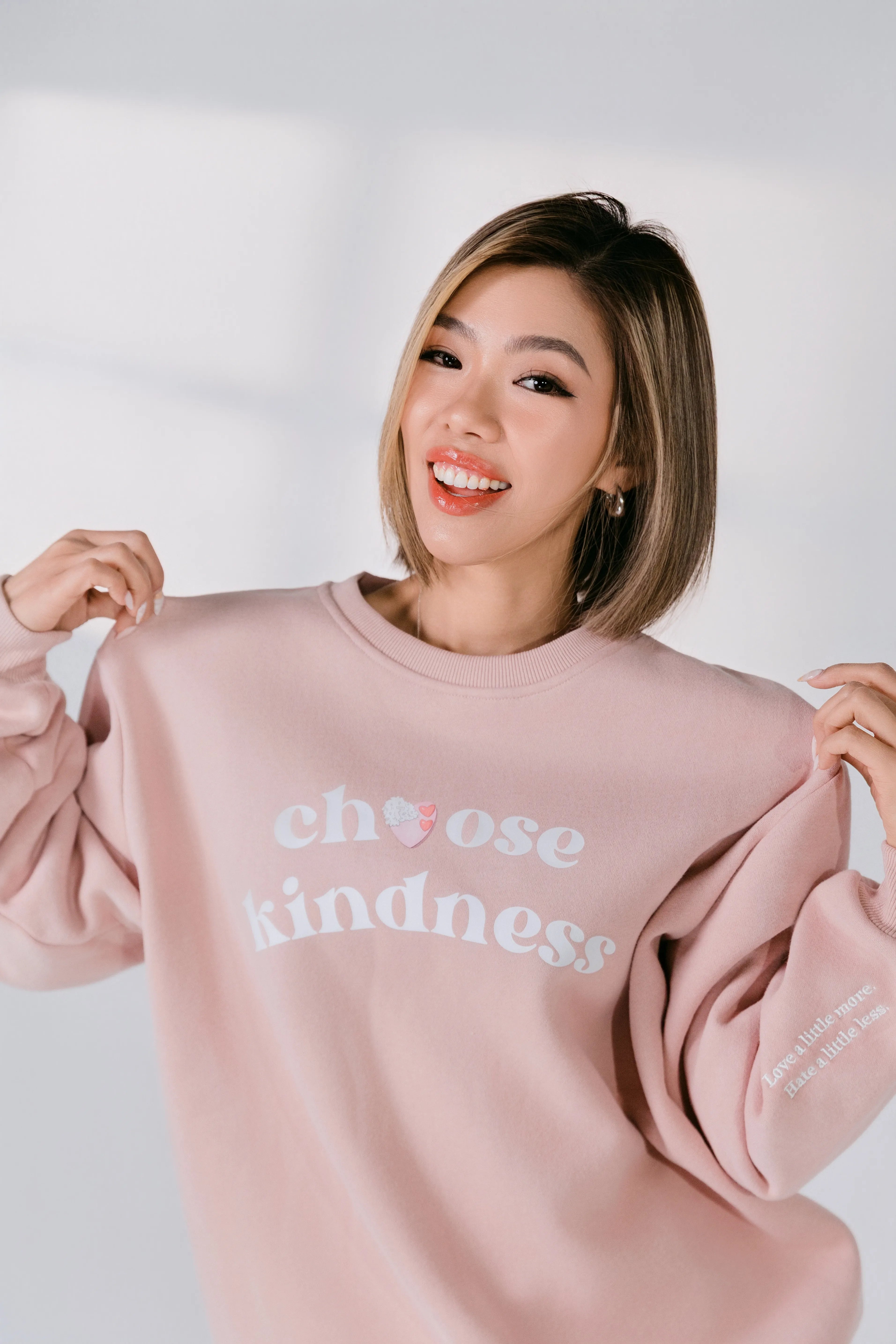 Person wearing a pink sweatshirt with 'choose kindness' text on a white background