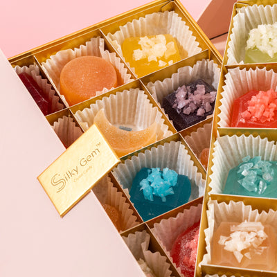 Top-down view of the 30-piece Silky Gem Gems Me Up crystal candy assortment inside a premium collector's box on a pink background