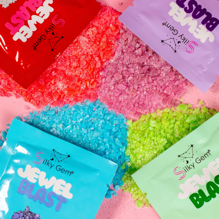 Four colorful pouches of Silky Gem® Jewel Blast sparkling sour popping candy, each featuring a different flavor and shimmering, crystal-like texture.