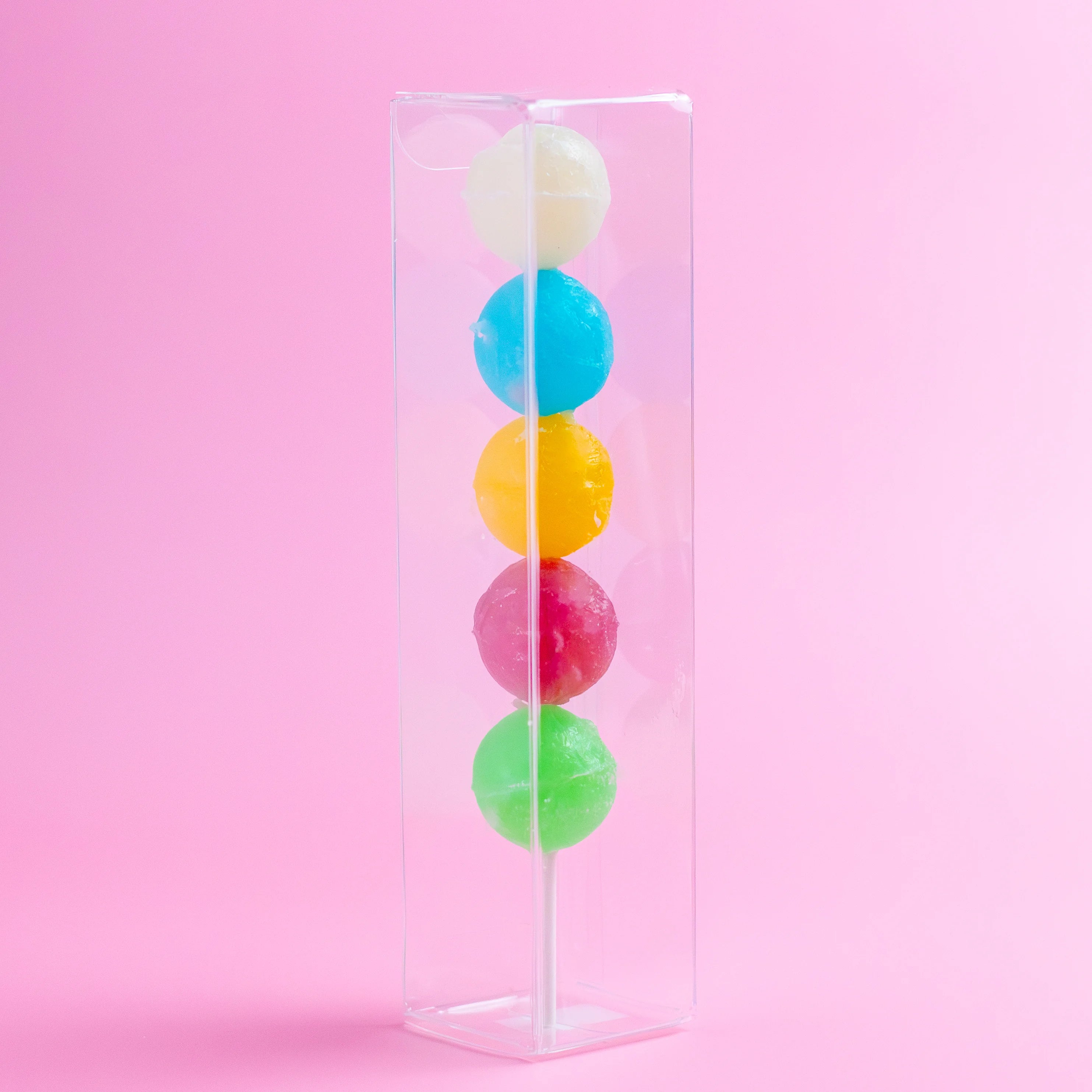 Colorful lollipops in a clear stand against a pink background
