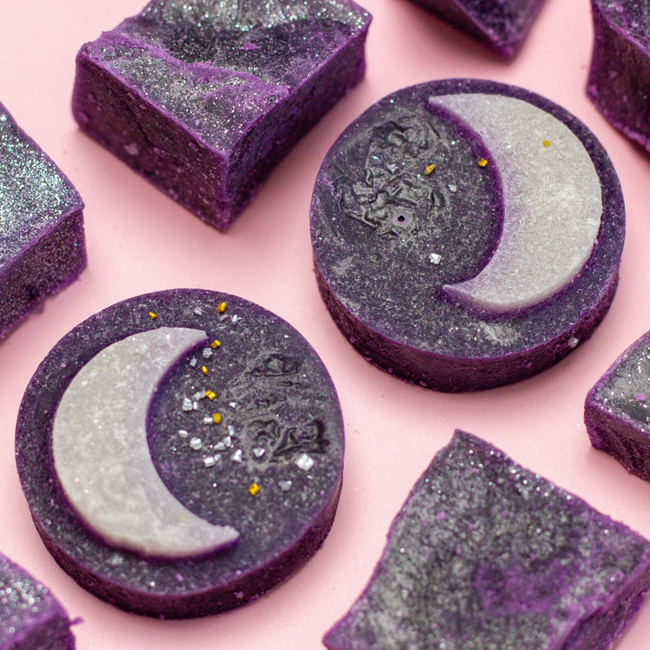 Purple soap bars with moon and star designs on a pink background