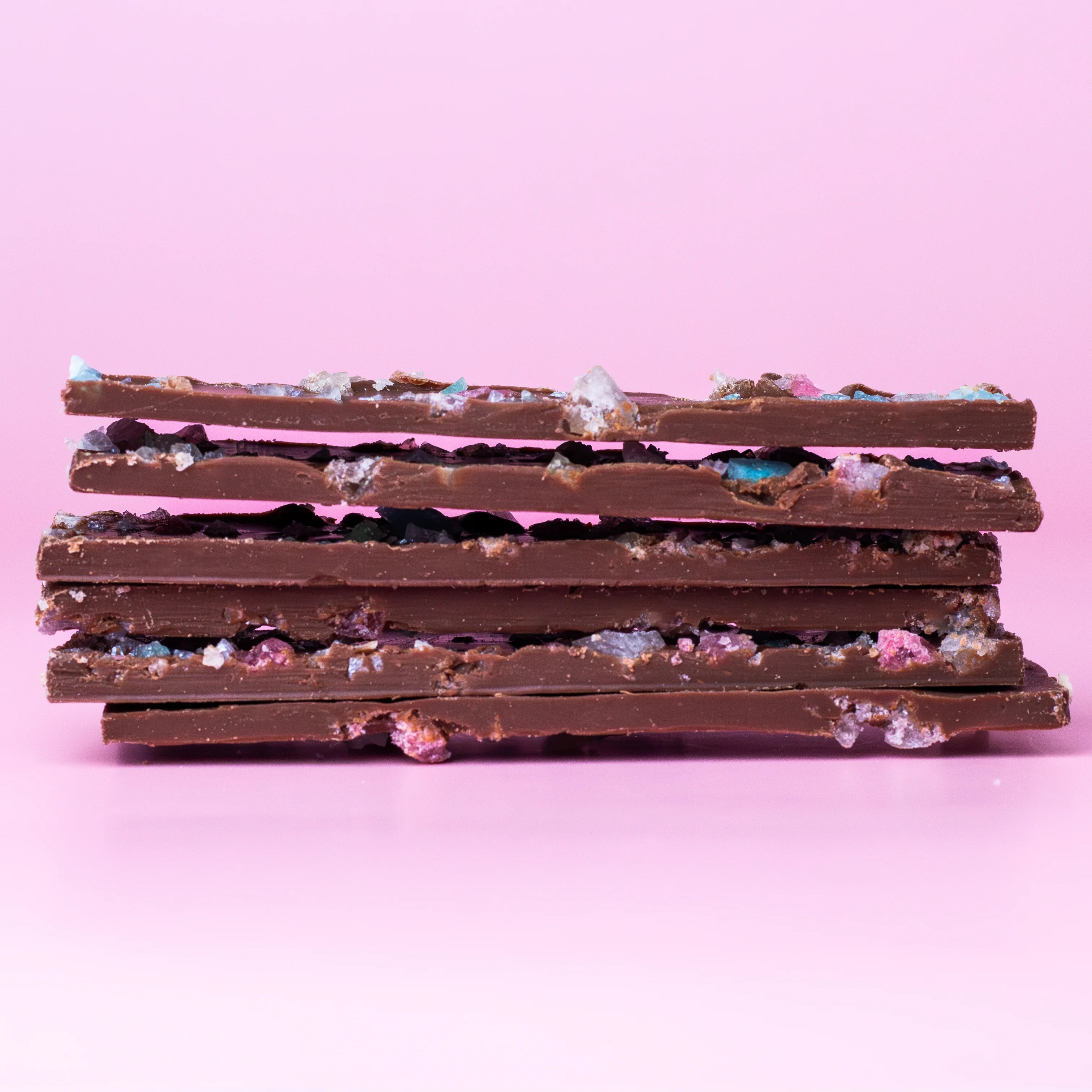 Stack of chocolate bars with visible toppings on a pink background