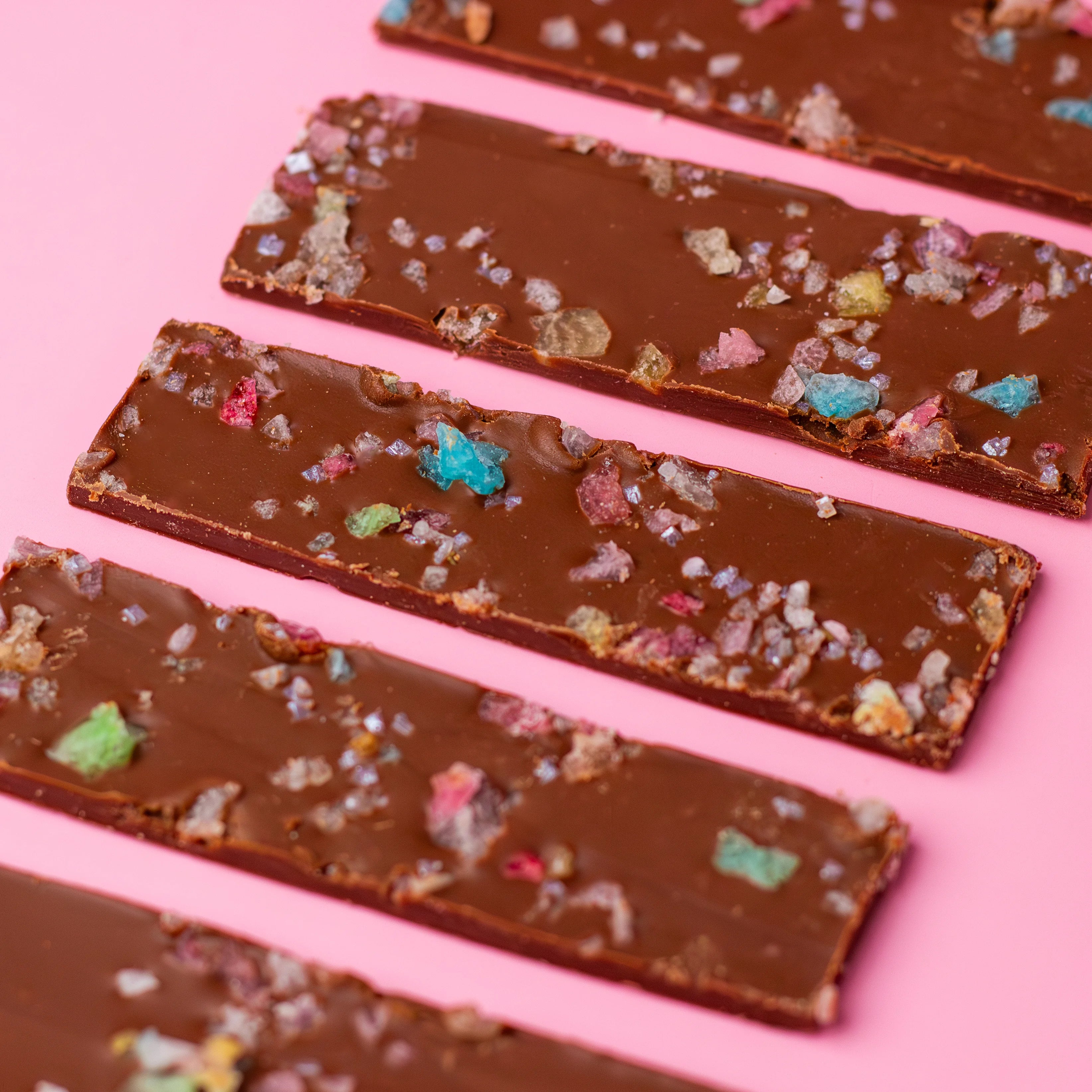 Chocolate bars with colorful toppings on a pink background