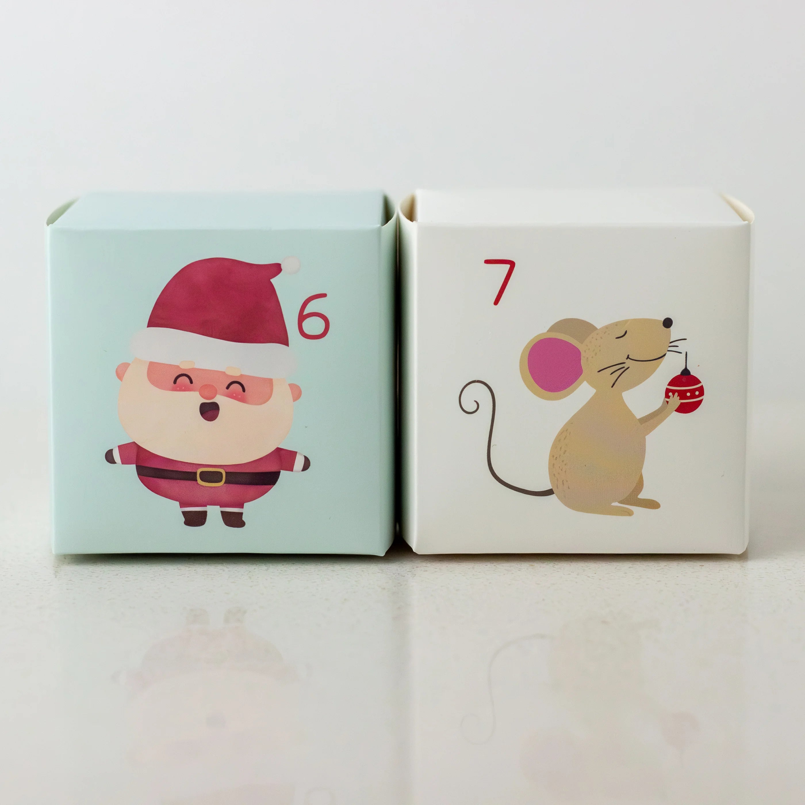 Two small boxes with Santa Claus and a mouse illustration on a light gray background