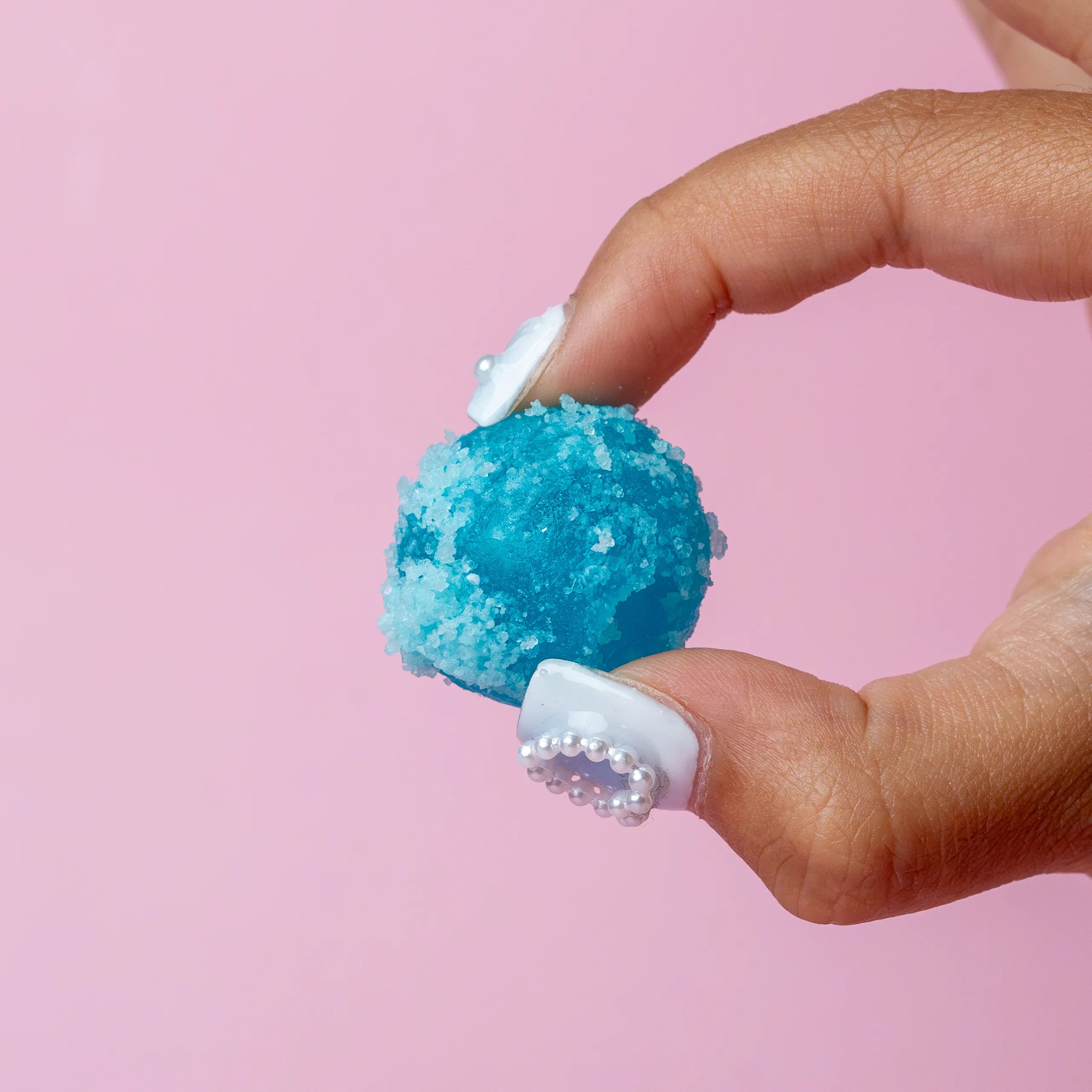 Hand holding a blue textured object against a pink background