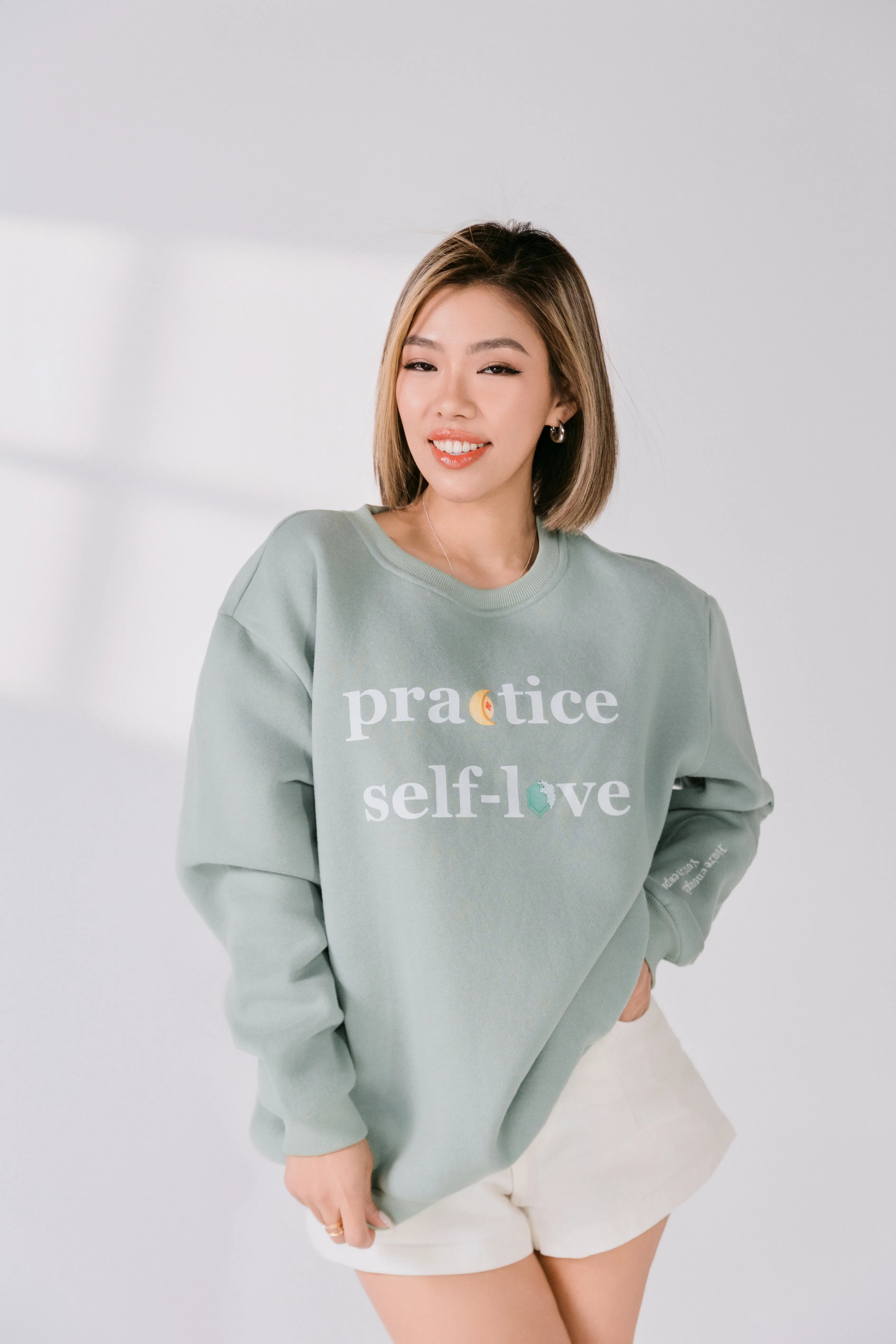 Model smiling while wearing relaxed fit sage green crewneck.