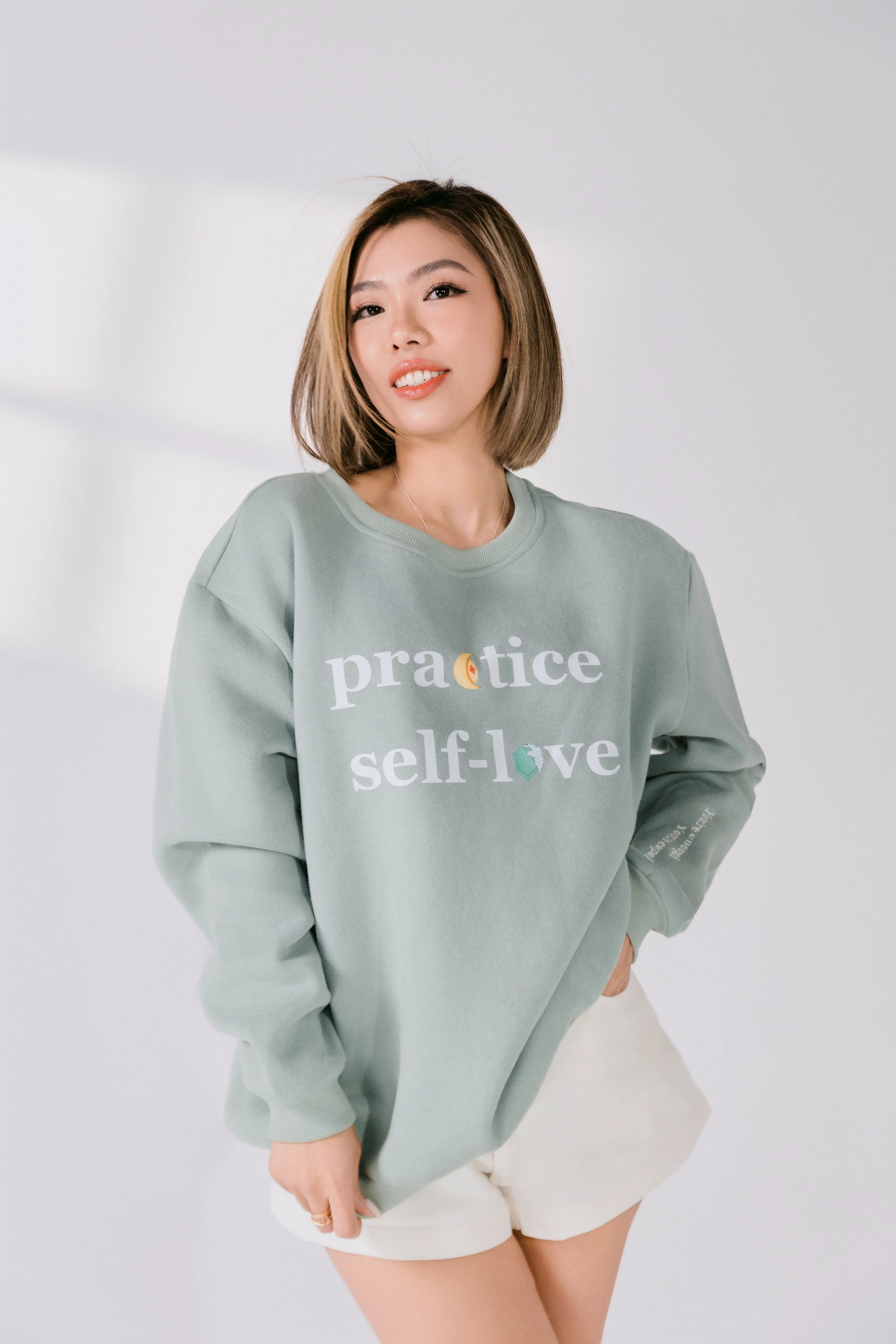 Full-body view of sage green cotton poly blend sweatshirt styled with light shorts.