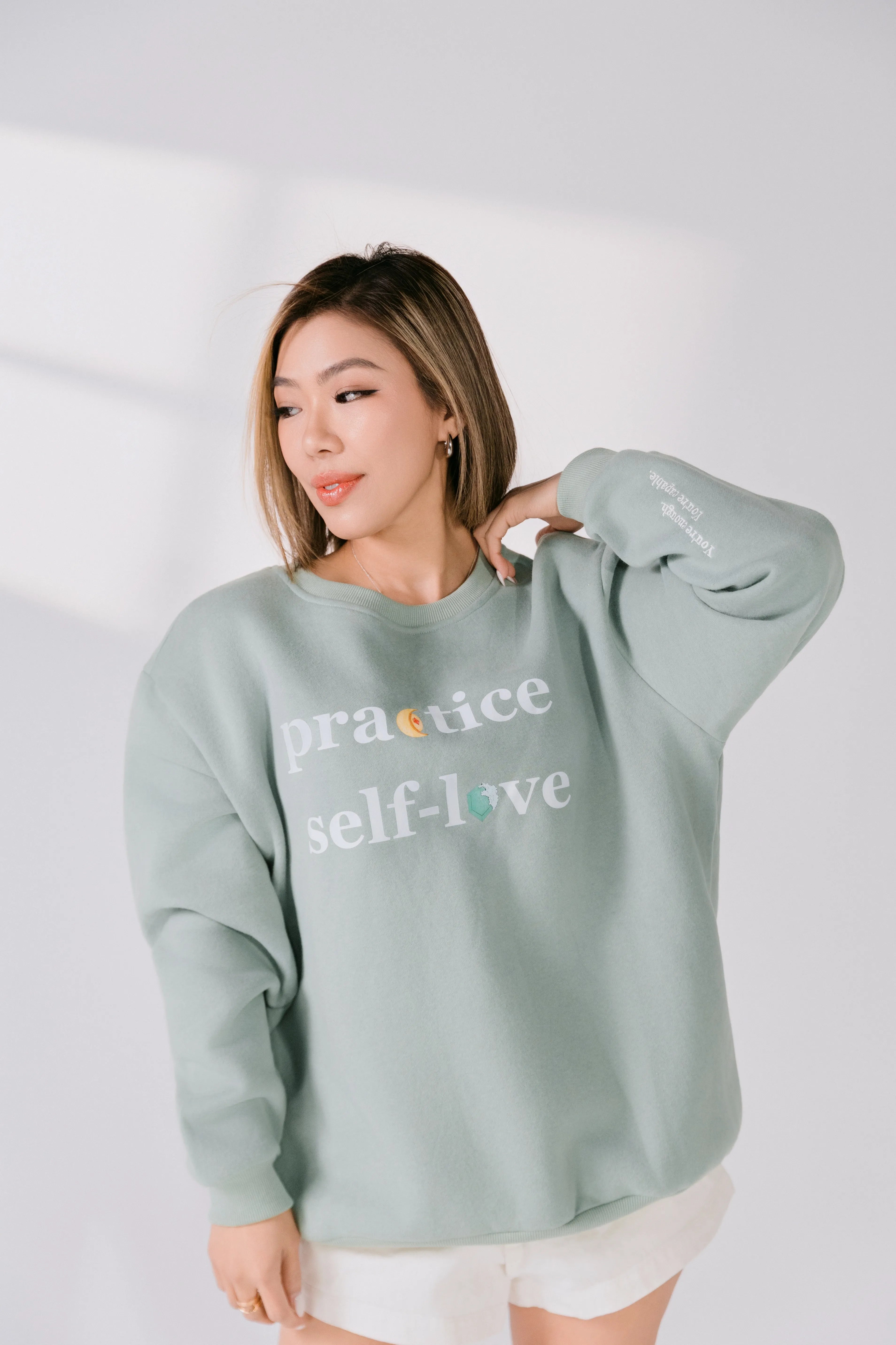Model wearing sage green “Practice Self-Love” Silky Gem crewneck, front view.