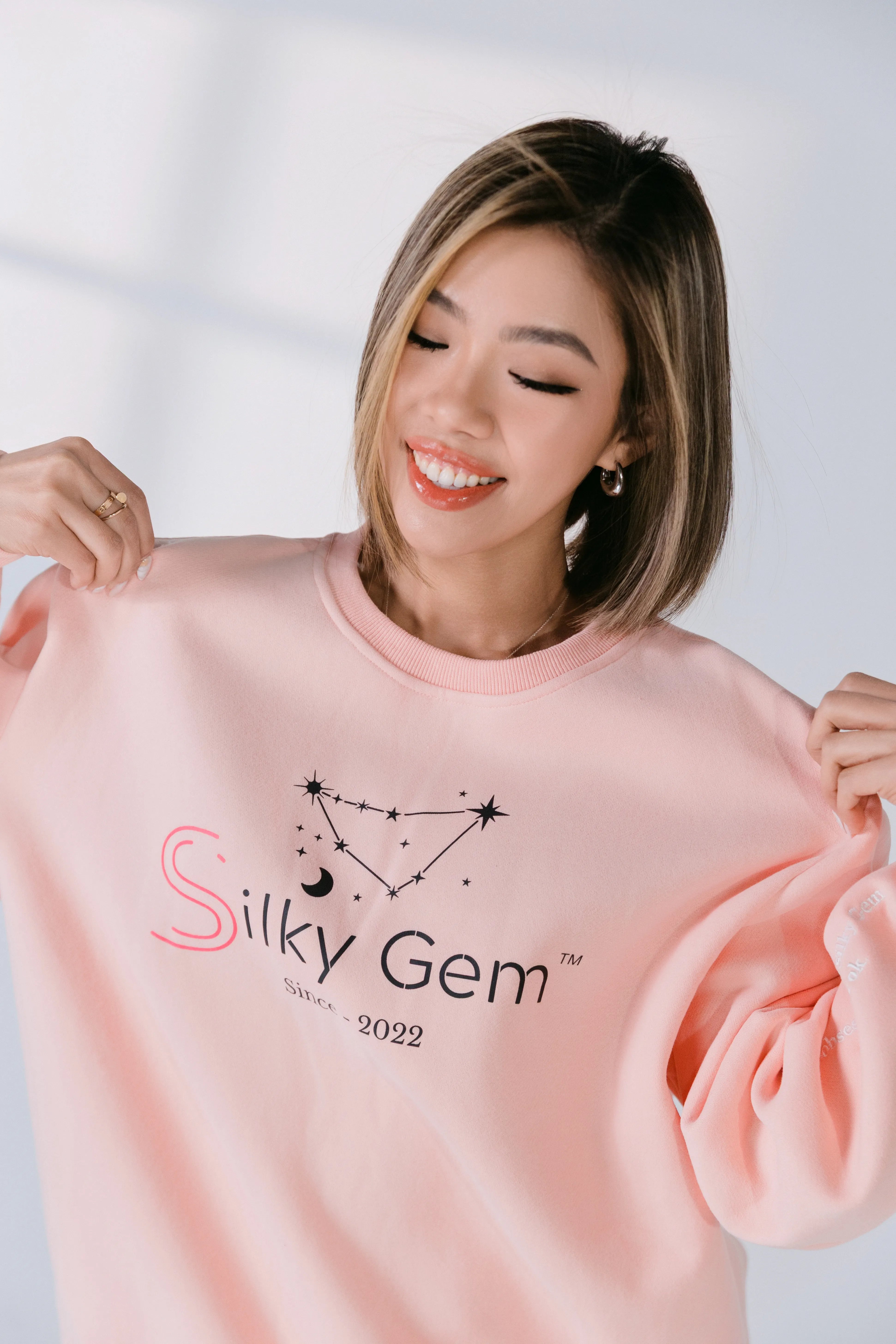 Model wearing blush pink Silky Gem signature crewneck with constellation logo.