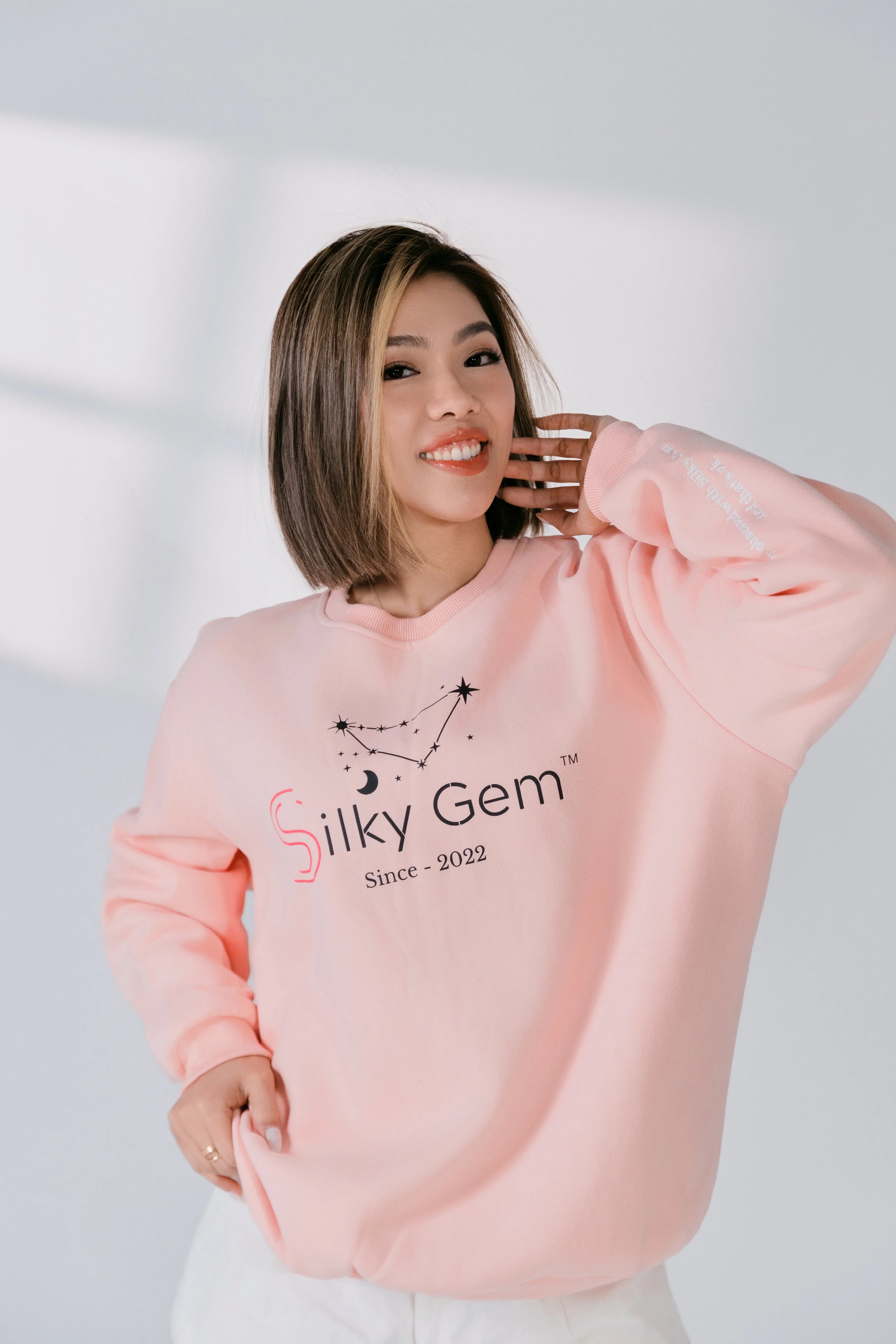 Person wearing a pink sweatshirt with 'Silky Gem' branding against a white background