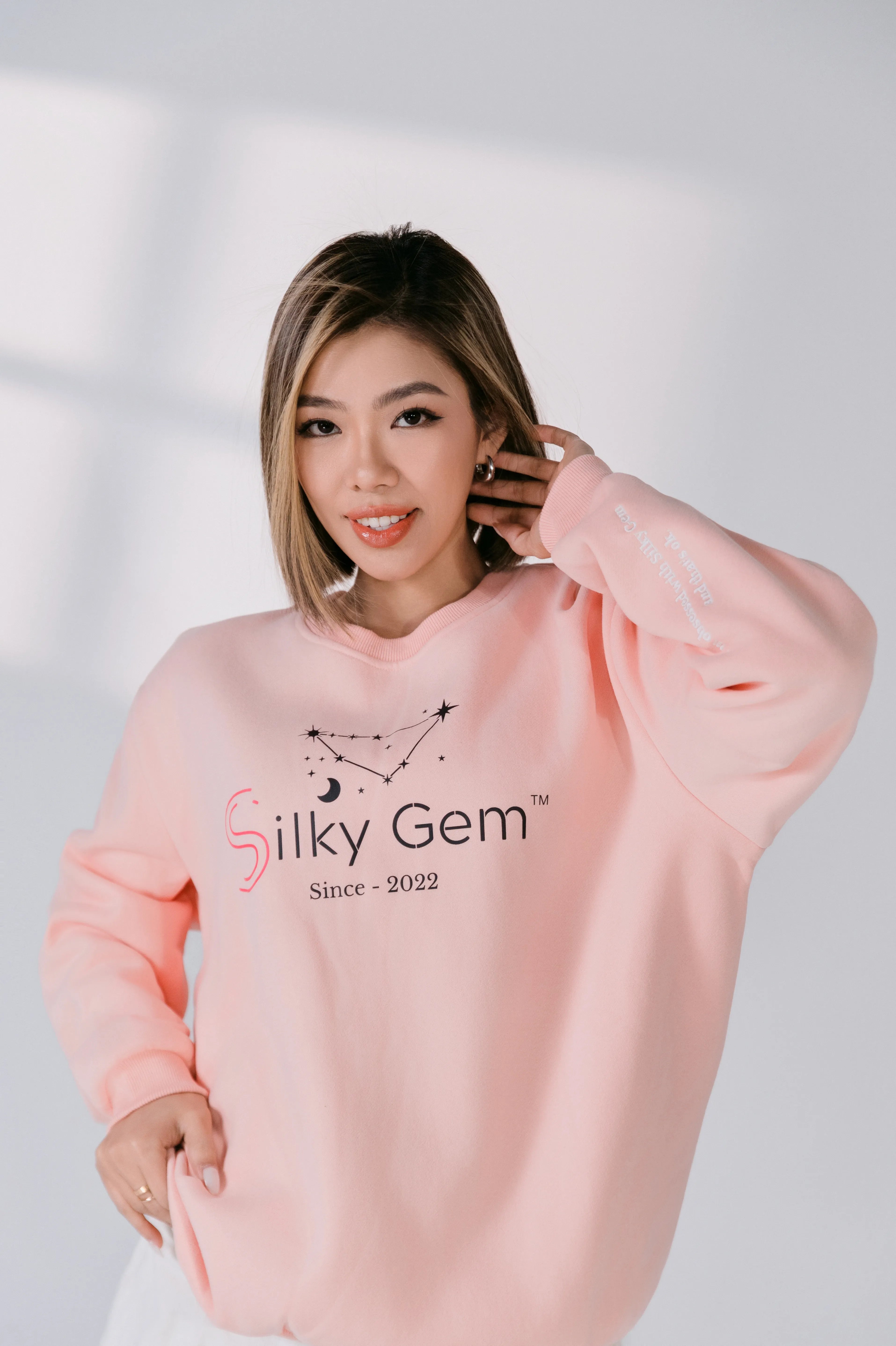 Person wearing a pink sweatshirt with 'Silky Gem' branding on a light gray background