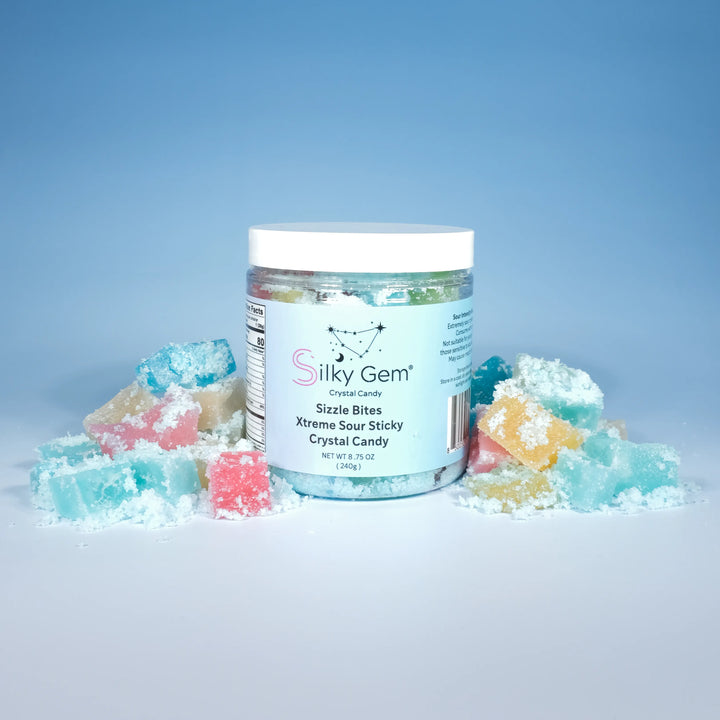 Jar of Silky Gem Sizzle Bites filled with mini crystal candies coated in sparkling sour sugar, surrounded by colorful cubes on a blue background.