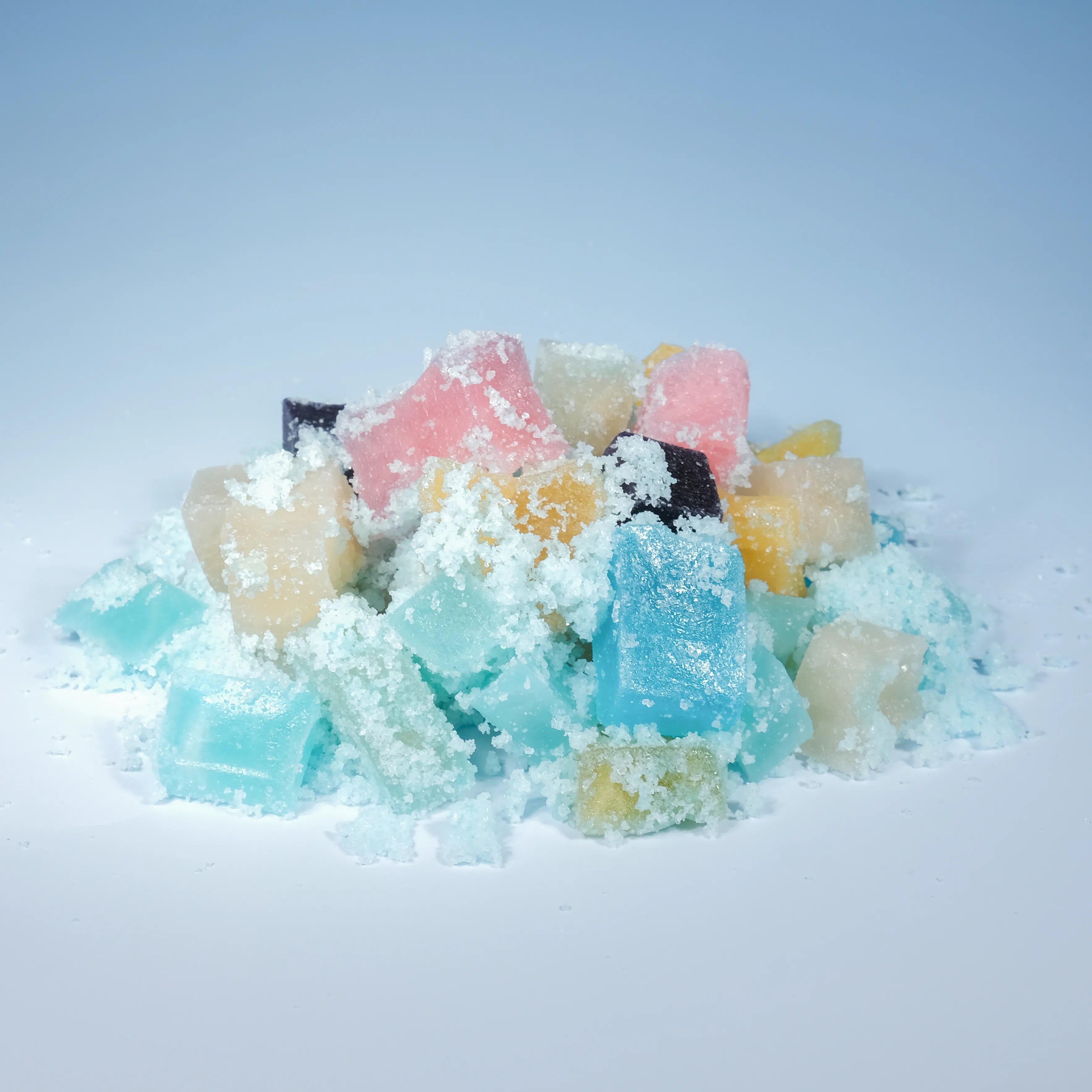 Assorted mini crystal candies with sparkling sour sugar arranged around an open jar against a soft blue backdrop.