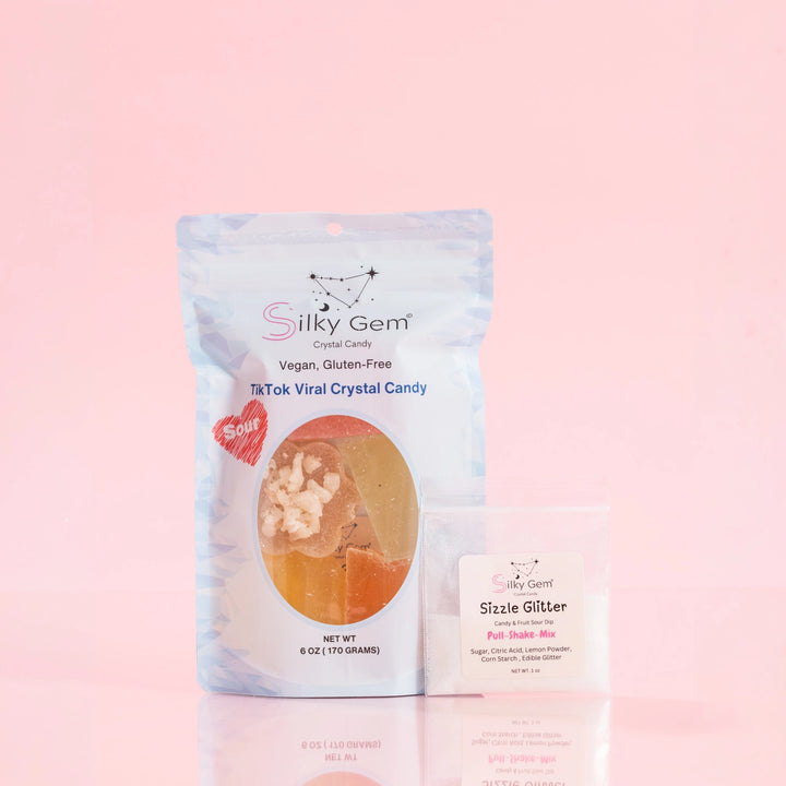 Silky Gem® Sour Bites 6oz pouch featuring a resealable design, displayed next to a small packet of Signature Sizzle Glitter on a pink background, highlighting the product as a TikTok viral crystal candy.