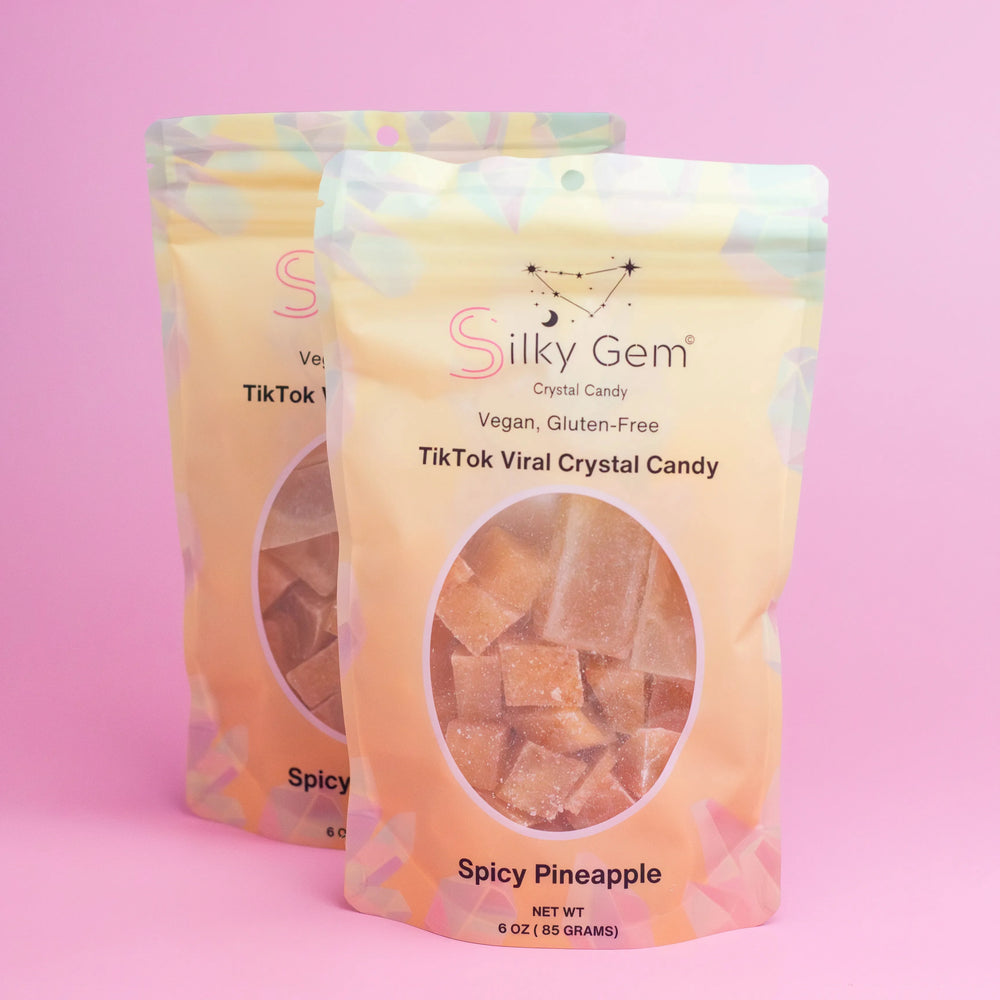 Two pouches of Silky Gem Spicy Pineapple Bites crystal candy on pink background