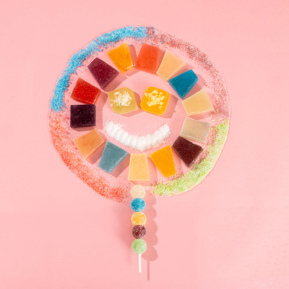 Artistic display of colorful Silky Gem crystal candies arranged in a smiling face shape on a pink background, featuring various signature cuts from the Starter Kit bundle.