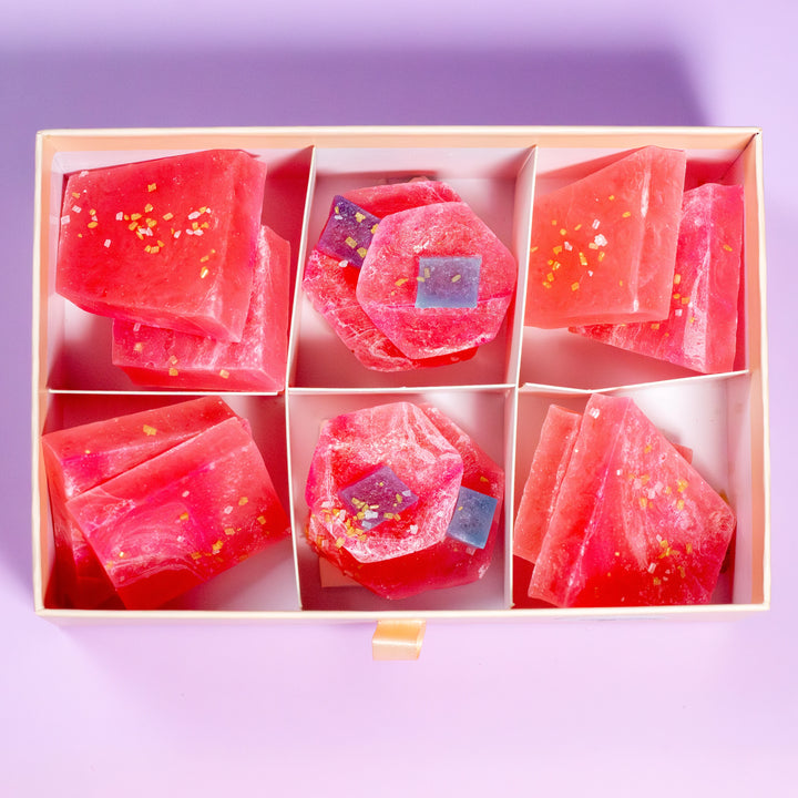Pink soap bars with glitter in a wooden box on a purple background