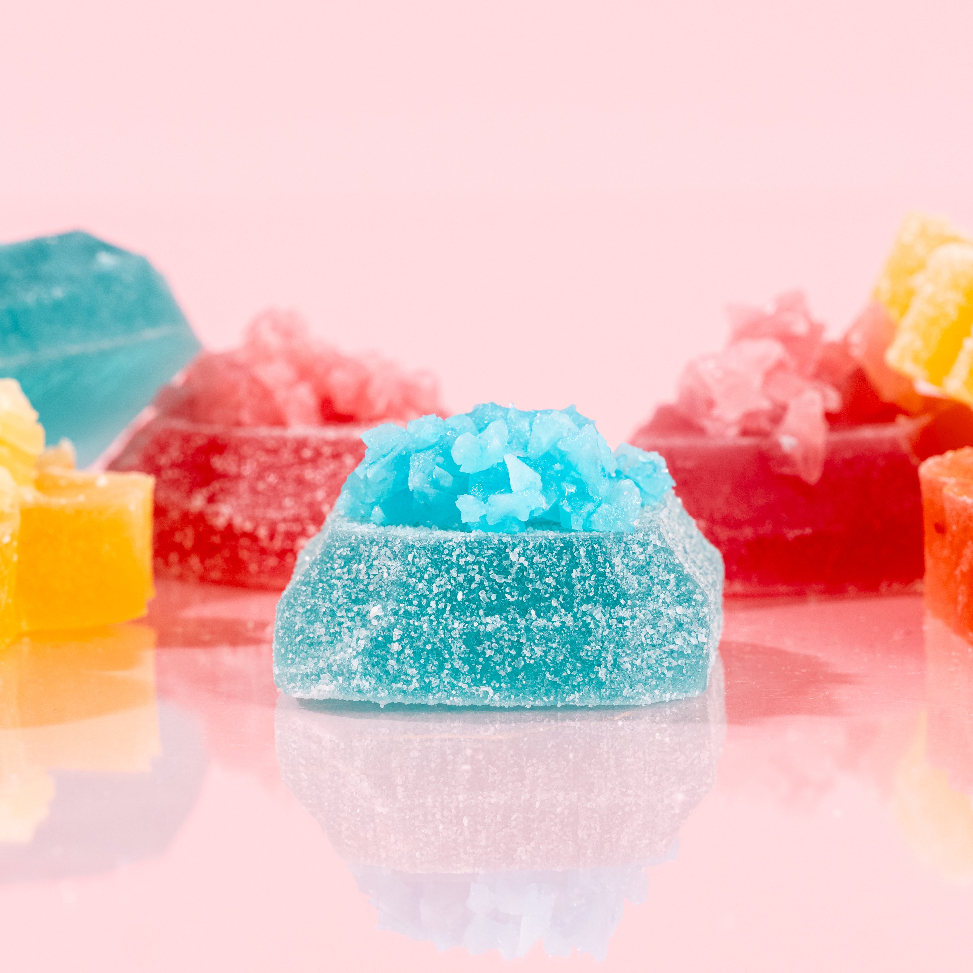 Close-up of a vibrant blue Silky Gem crystal candy piece from The Golden Lava collection on a pink background.