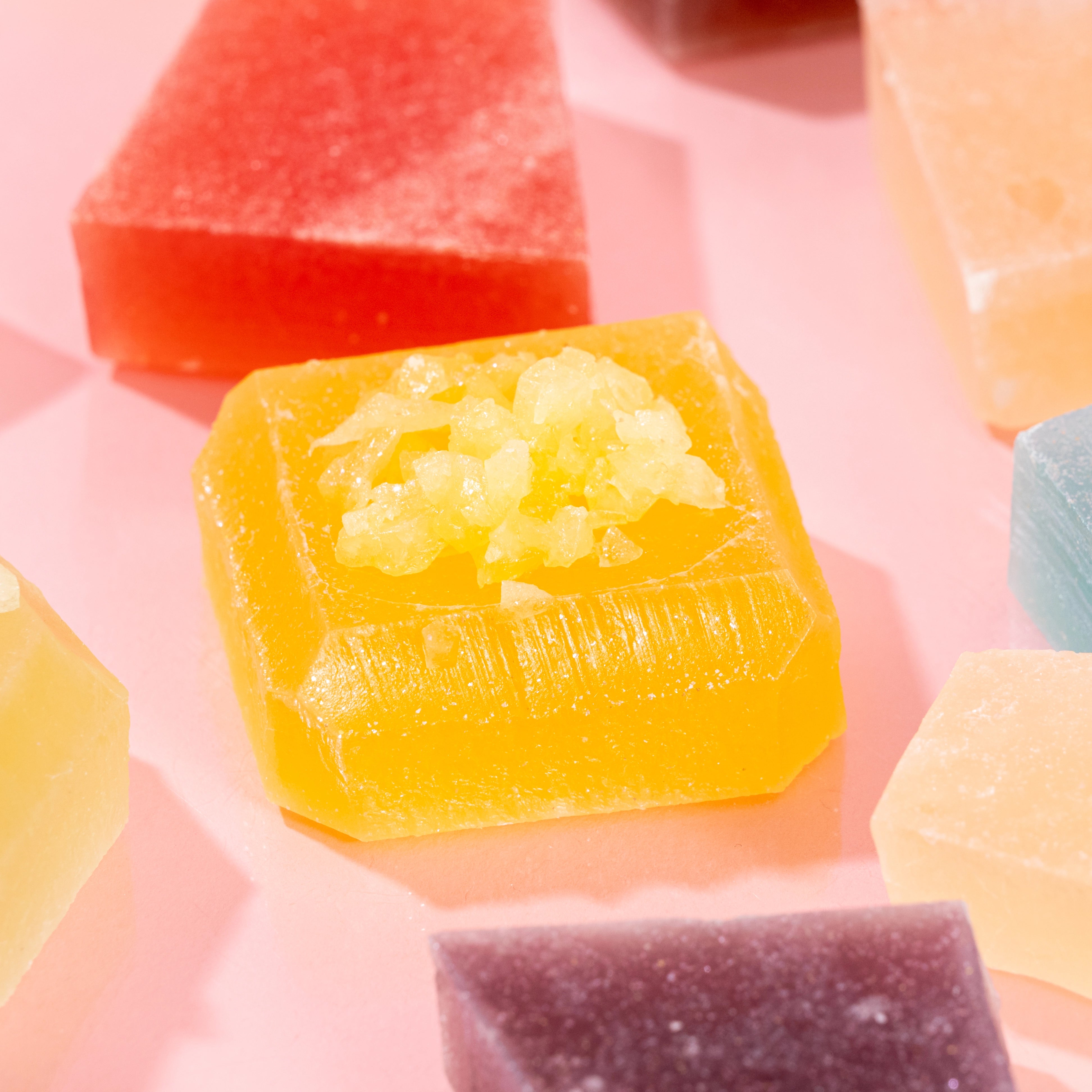 Close-up view of handcrafted Silky Gem® crystal candies, featuring a textured, jewel-toned appearance with a translucent, firm, jelly-like center, displayed on a pink background.