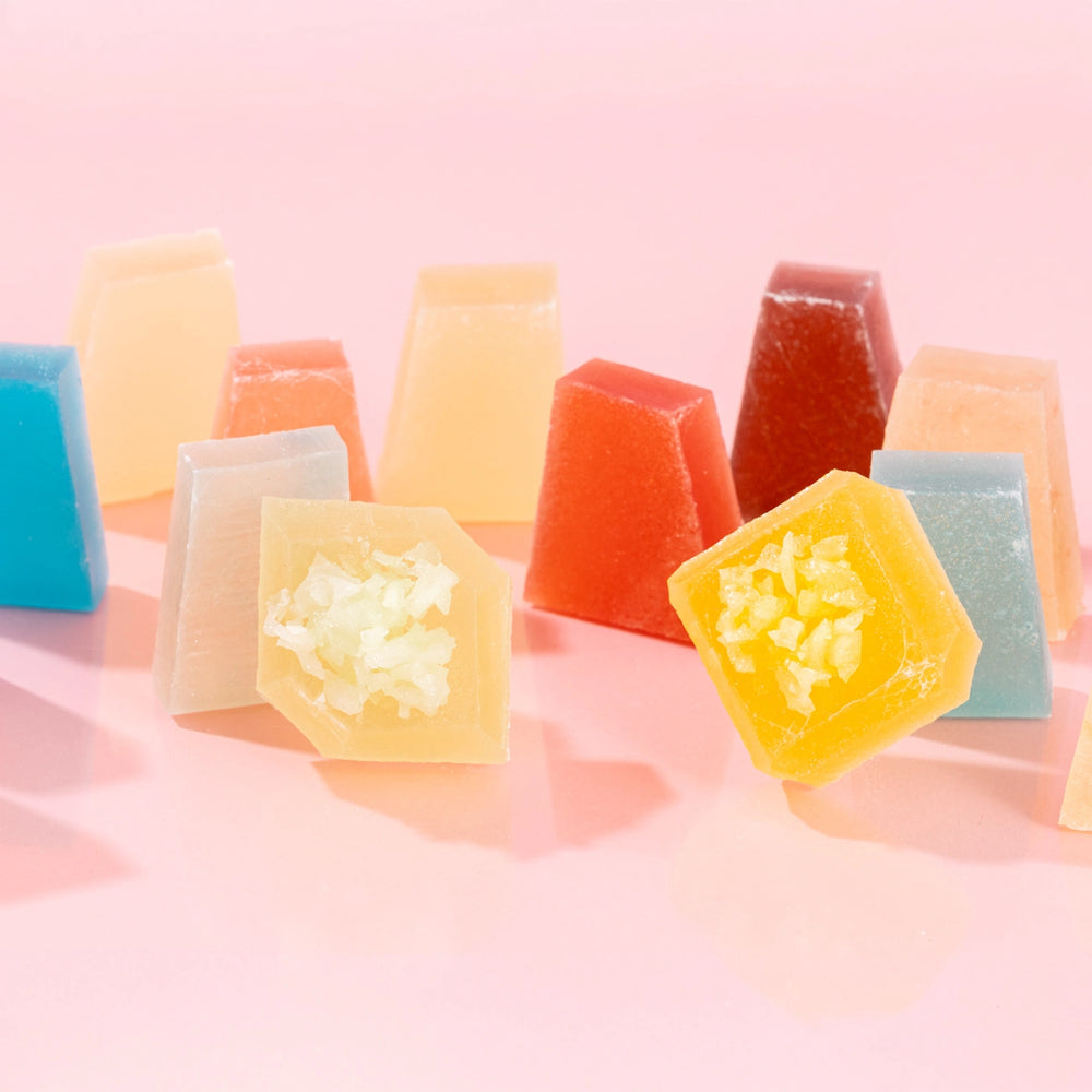 Close-up of assorted, vibrant Silky Gem crystal candy pieces from the Treasure Box collection, featuring various shapes and signature cuts on a pink background.