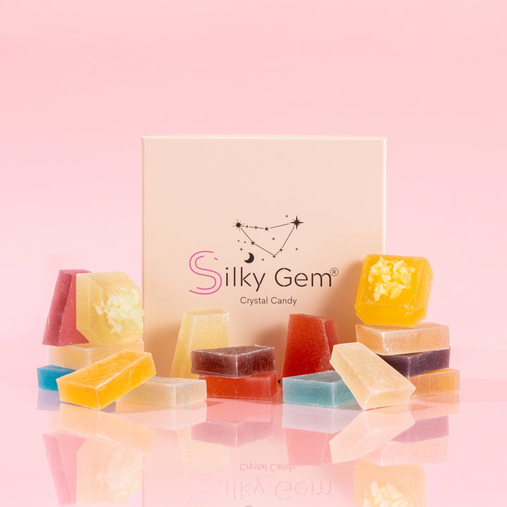 Assorted Silky Gem crystal candy pieces in various shapes and signature cuts from the Treasure Box collection, displayed with a branded gift box on a pink background.