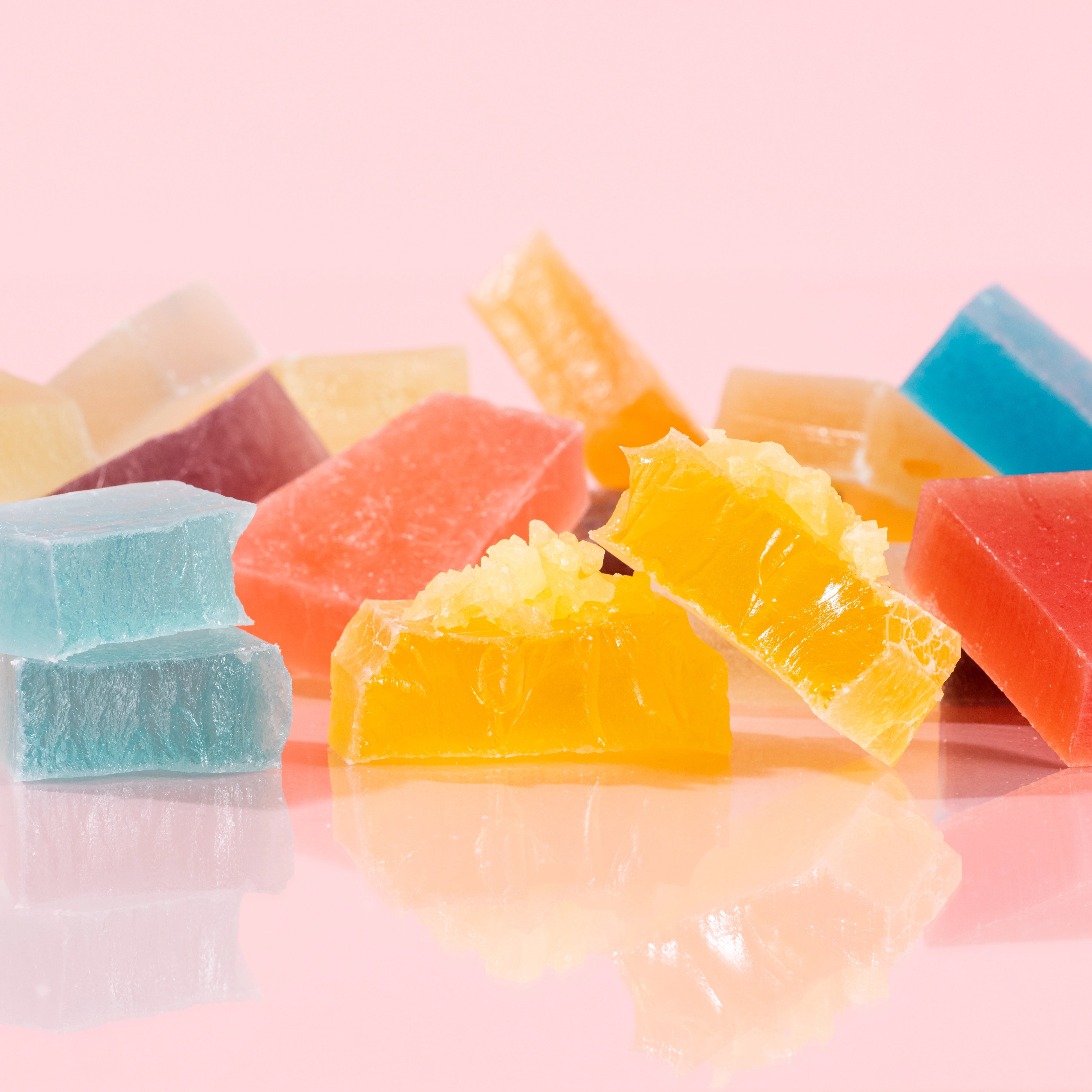 Close-up of vibrant, crystal-cut candy pieces from the Treasure Box collection, with some pieces cut in half to reveal the signature firm, jelly-like center, displayed on a pink background.